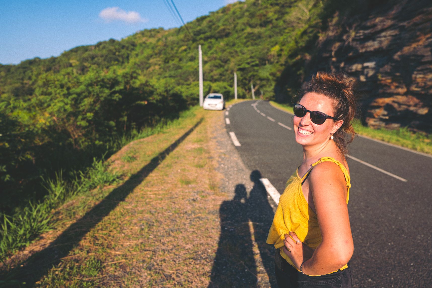 Portrait du côté gauche, la fille regarde l'appareil photo et sourie. Derrière la route continue dans les montagnes arborées