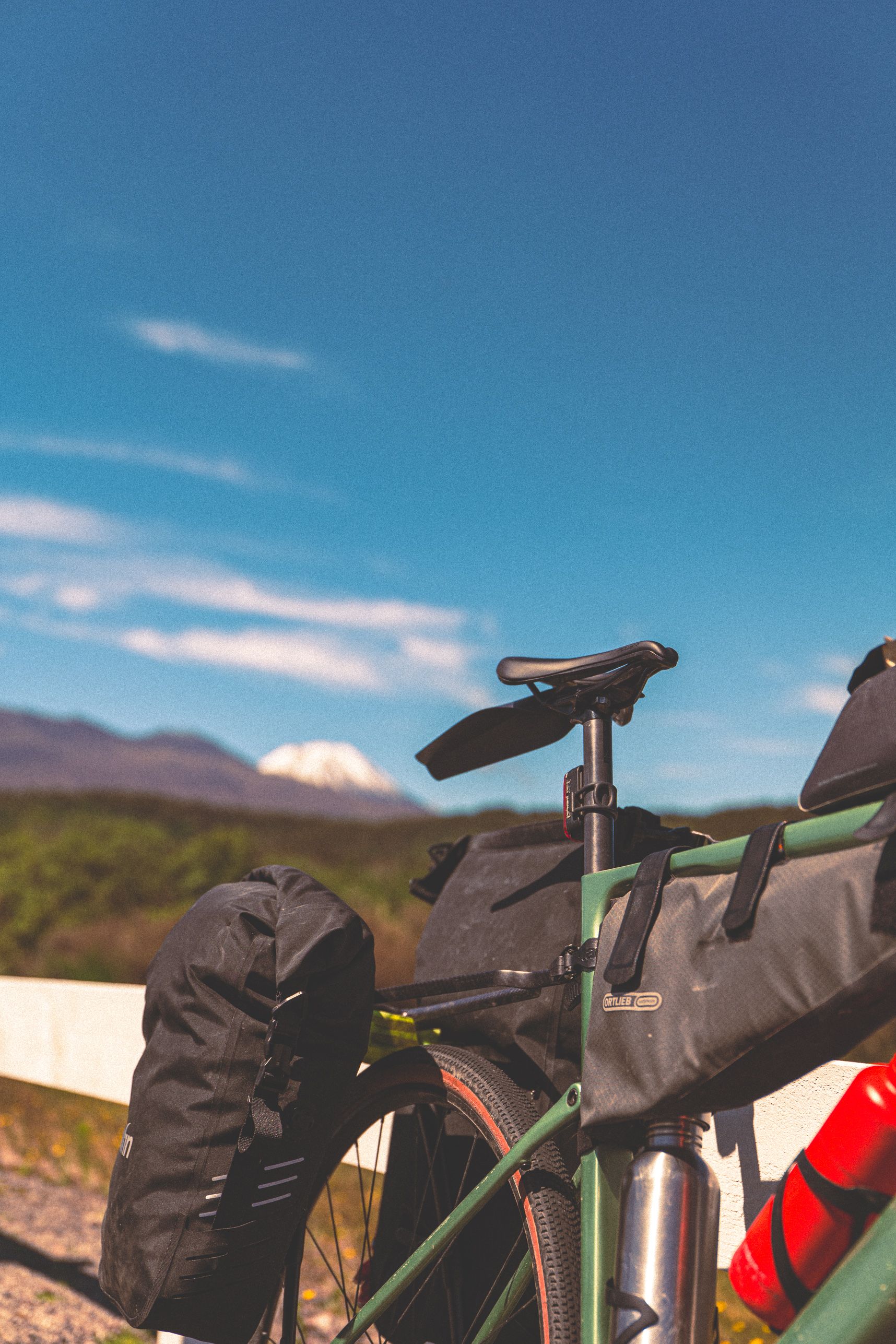 Un vélo charger de sacoches pour faire du bikepacking. La selle pointe vers la droite. Derrière une montagne enneigée