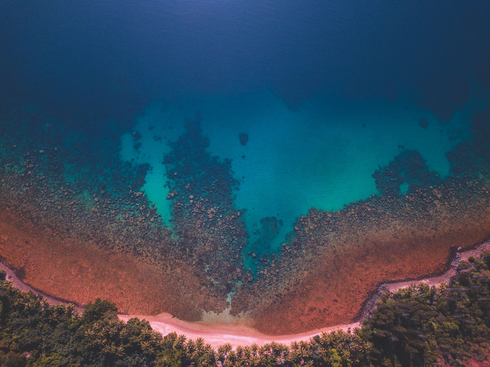 Vue de drone sur la plage de l'îlot Némou. On y voit les coraux jusqu'à disparaitre dans le bleu foncé de la mer