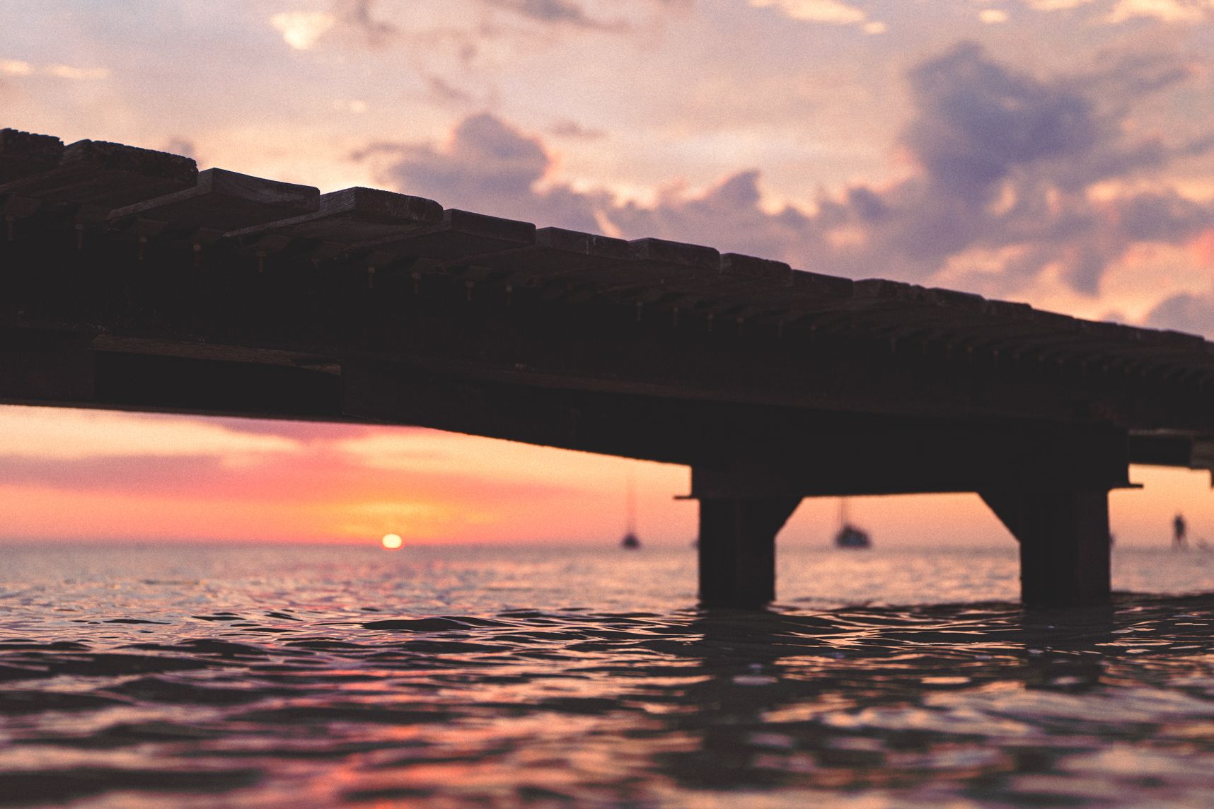 En dessous du ponton le soleil donne ses dernières lueurs. Les couleurs orangées reflètent sur la mer.
