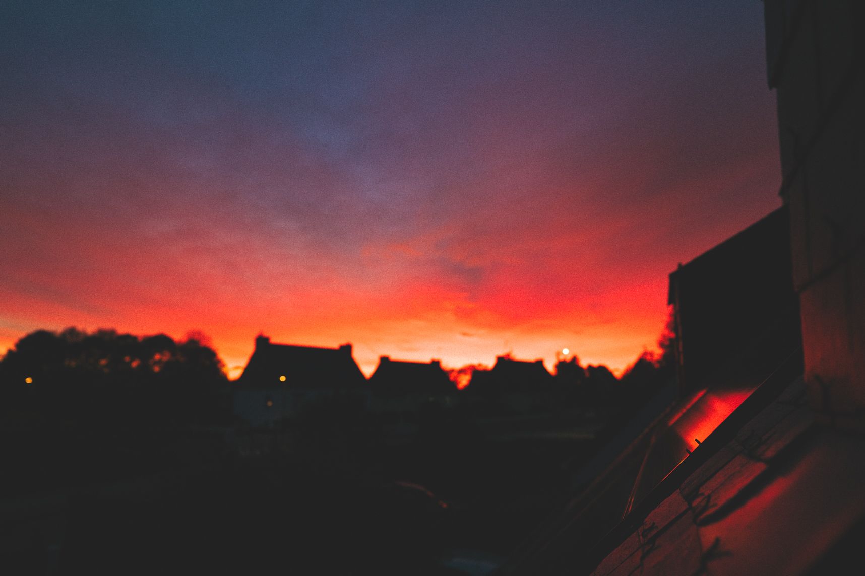 Le soleil est couché. On distingue des maisons dans la ligne d'ombre. Les nuages sont roses orangés