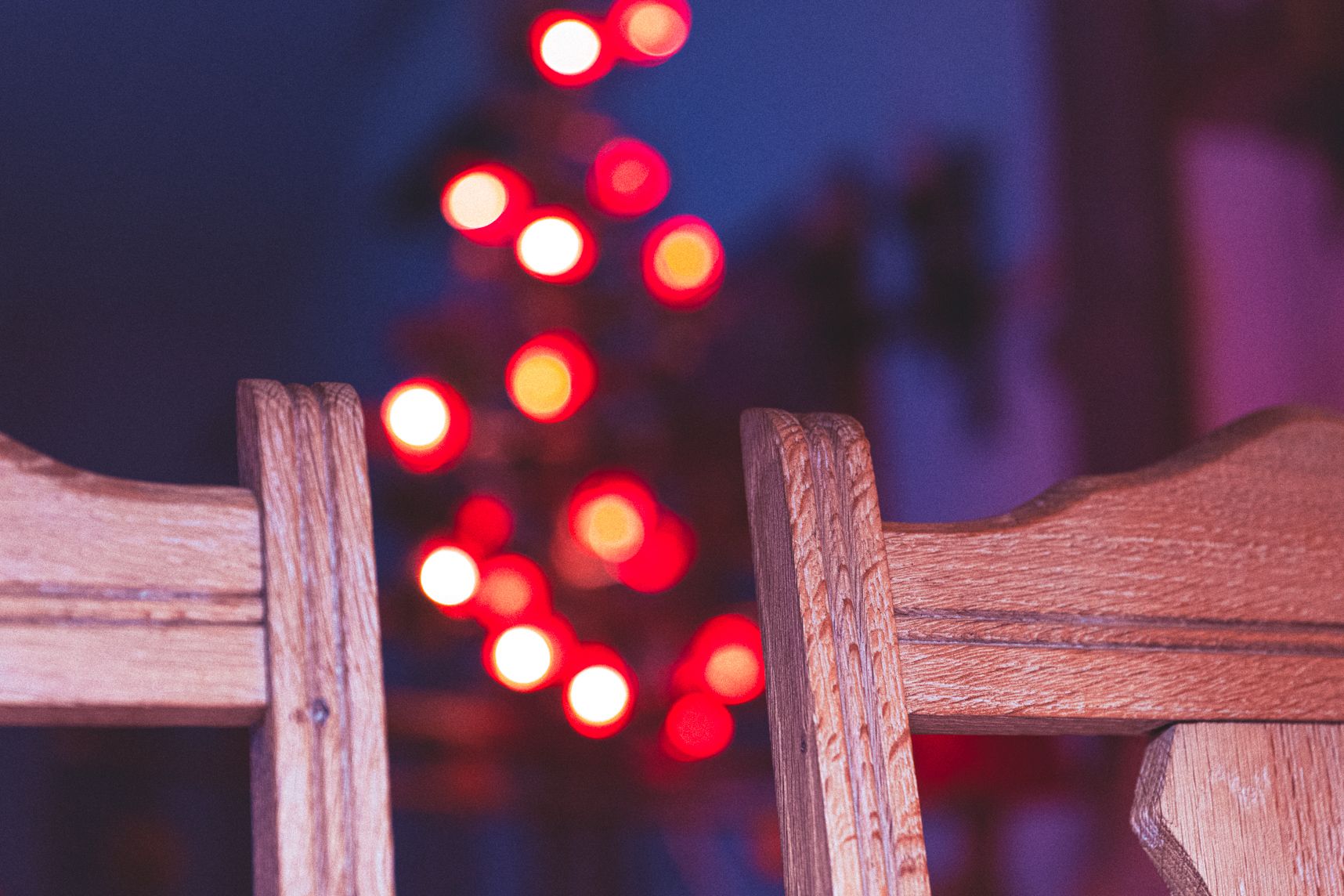 Deux parties de dossiers de chaise au premier plan. Entre les deux dans le bokeh, les lumières du sapin de Noël. L'arrière plan est sombre avec une teinte bleu et violet