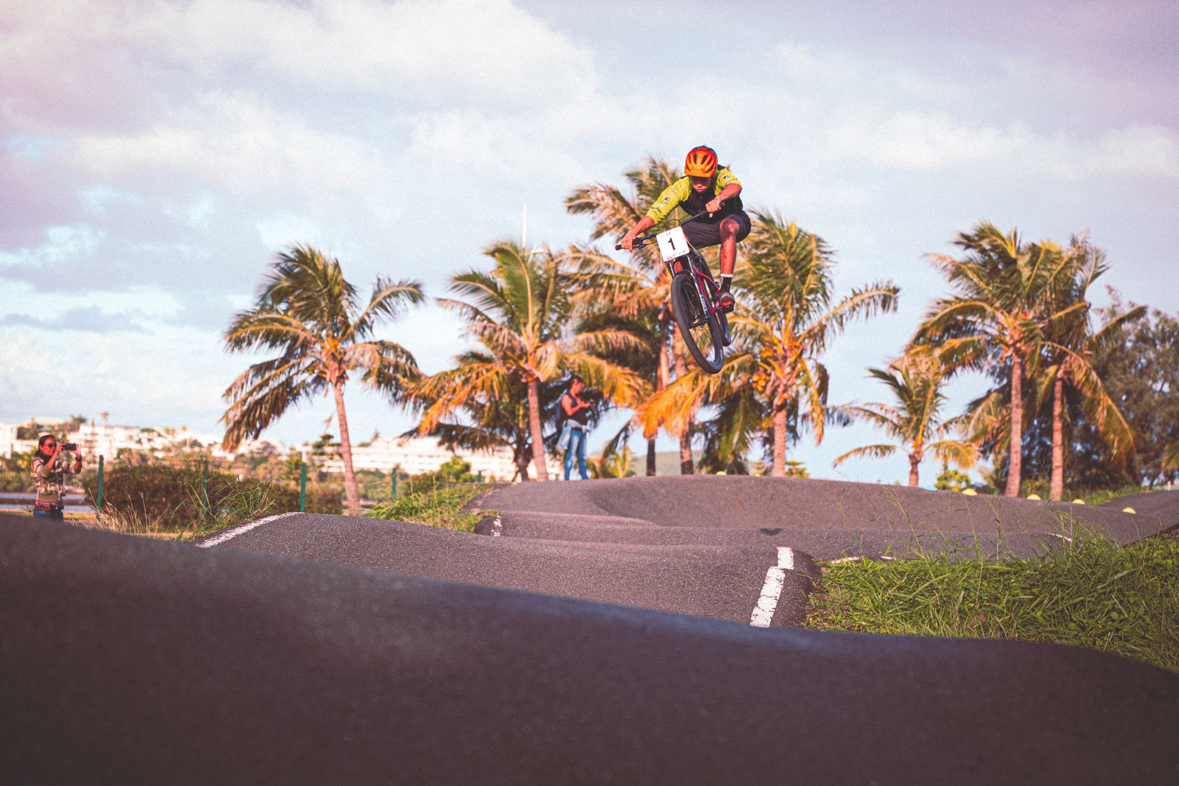 Dans l'alignement du parcours de Pumptrack, le cycliste est en train de voler. Derrière les palmiers