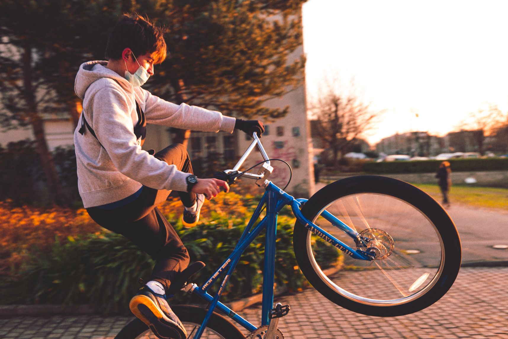 Une personne faisant des figures en wheeling sur son vélo bleu. Le genou gauche est sur la selle, la jambe droite à l'opposé. Le soleil va se coucher, les couleurs sont chaleureuses