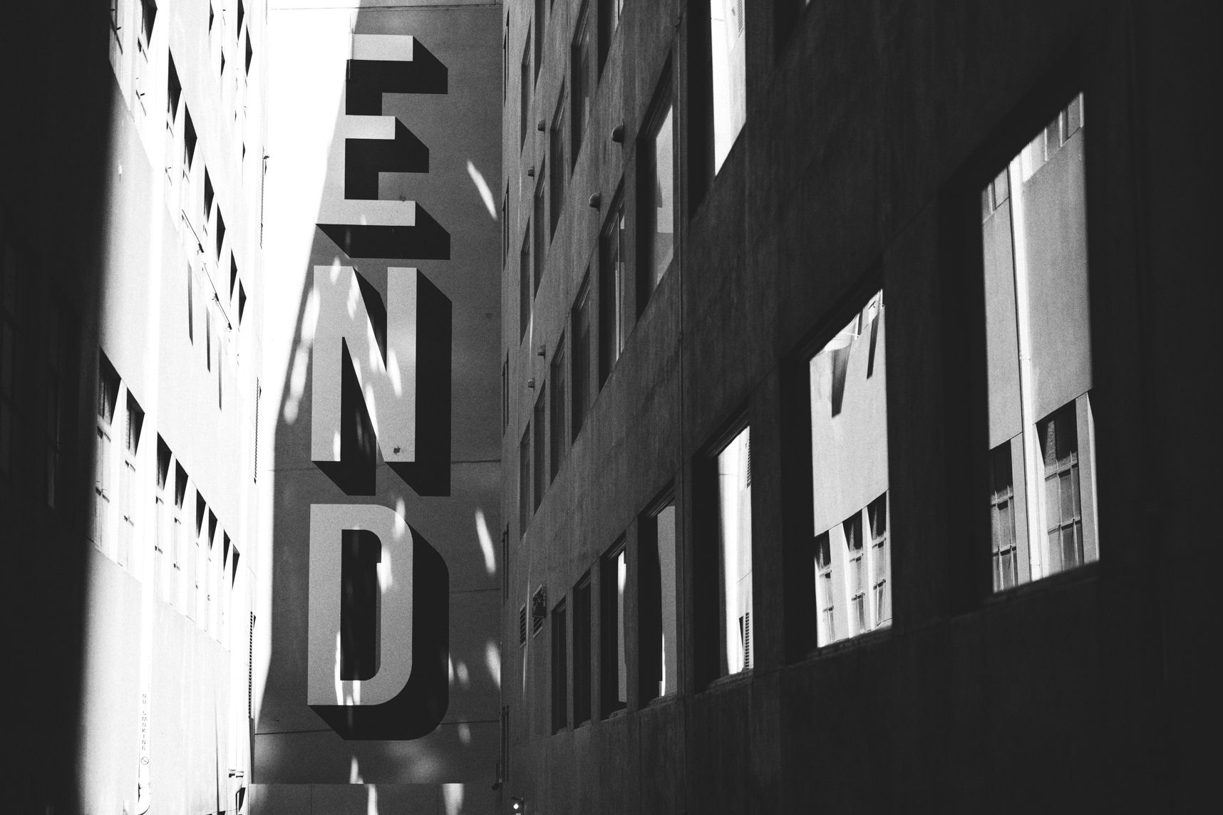 Rue étroite de Melbourne en noir et blanc. Sur la droite les fenêtres reflètent le bâtiment opposé. À la fin de la rue un mur avec marqué END