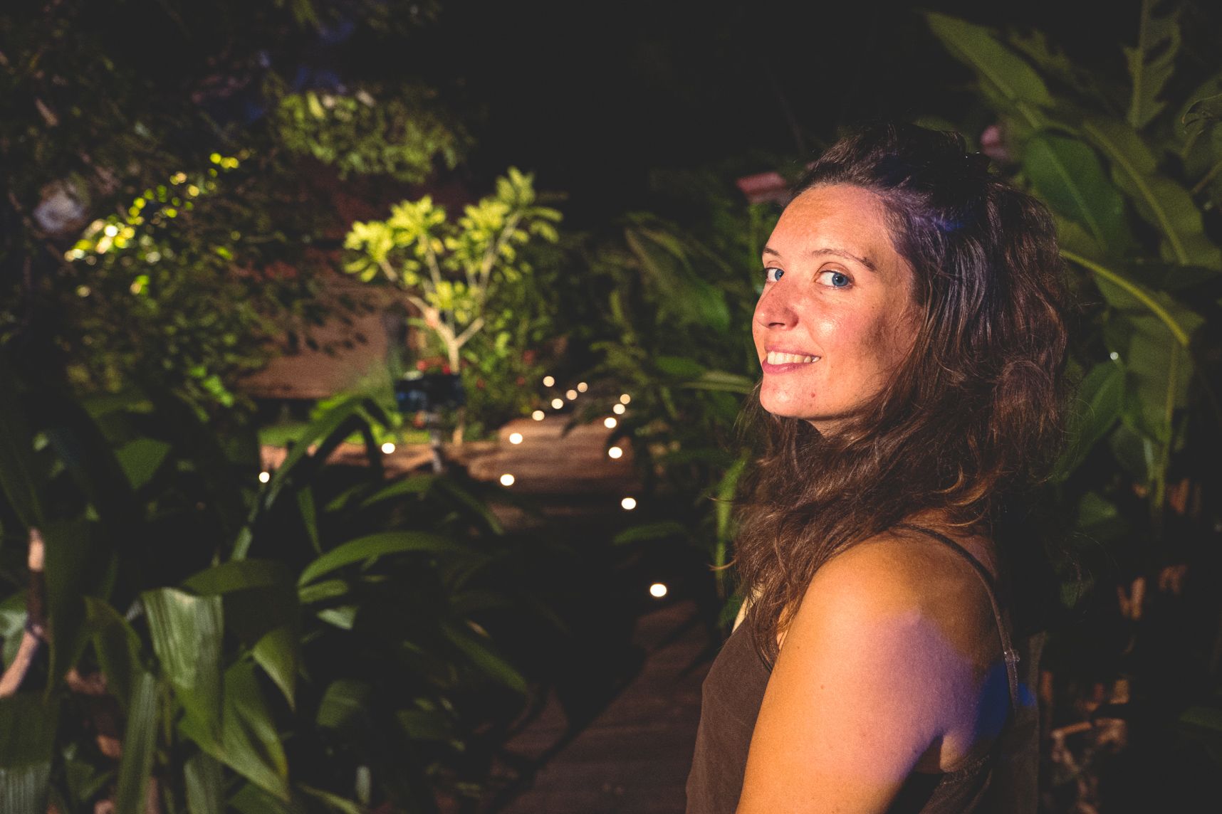 De profil, la femme regarde le photographe du coin de l'oeil. Derrière le chemin illuminé dans la jungle.