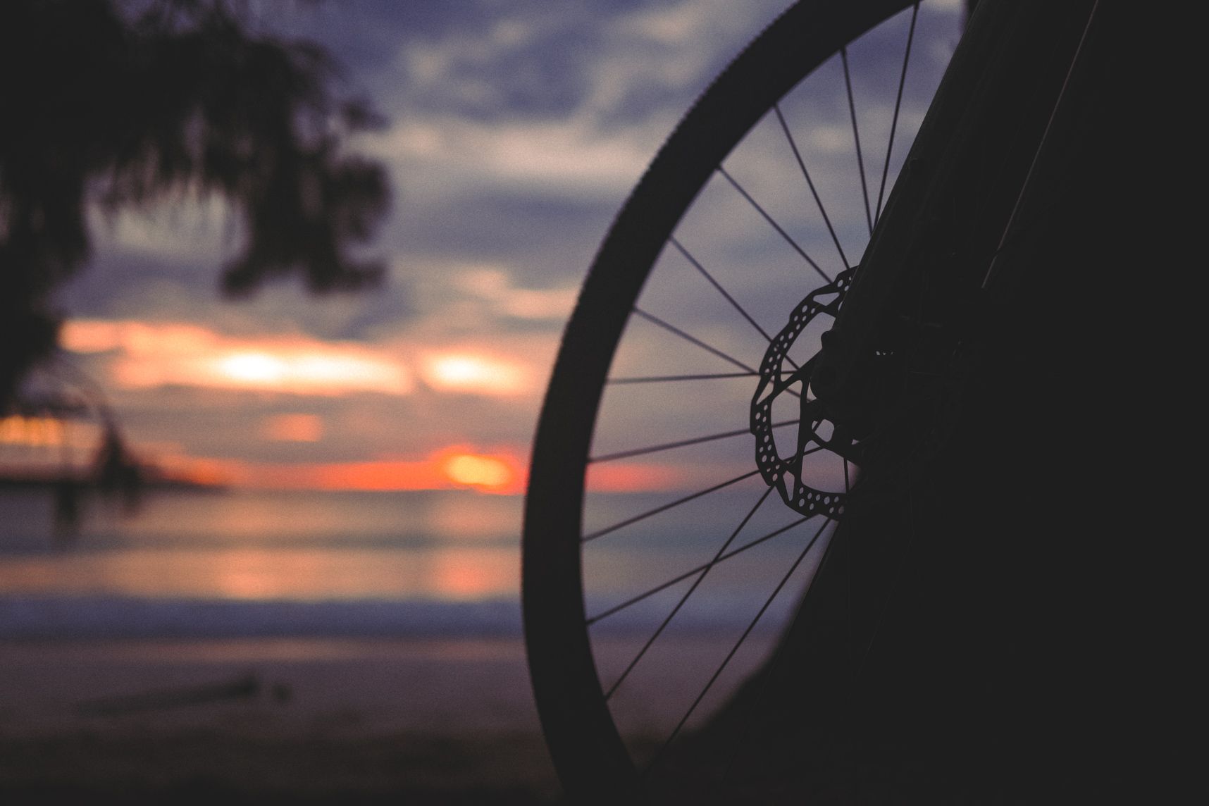 Premier plan une moitié de roue de vélo dans l'ombre. En arrière plan dans le flou, le coucher de soleil sur la mer à travers les nuages