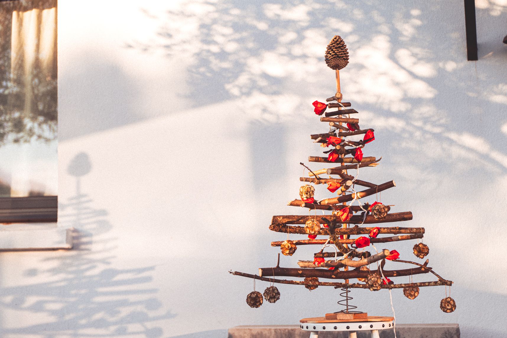 Sapin de Noël fait à partir de vielle branche, bouts de bois et vieux sommier. Des guirlandes en forme de fleur orange enlace le sapin. Des boules en copeau de bois sont accrochées