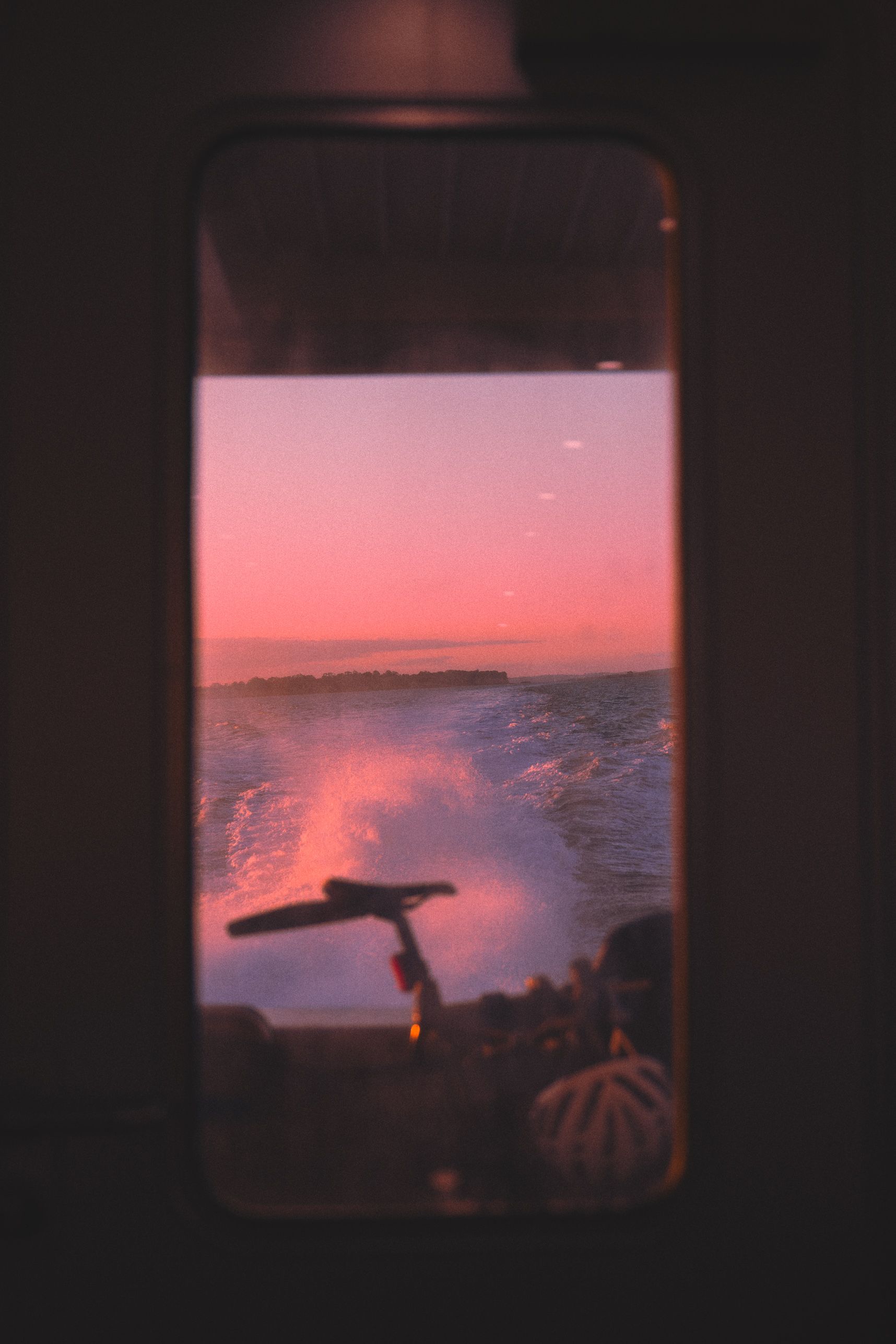 Fenêtre de l'arrière du bateau pour aller à Pine Harbour. Le soleil se couche. À travers on voit la selle d'un vélo, les remous de l'eau et le paysage