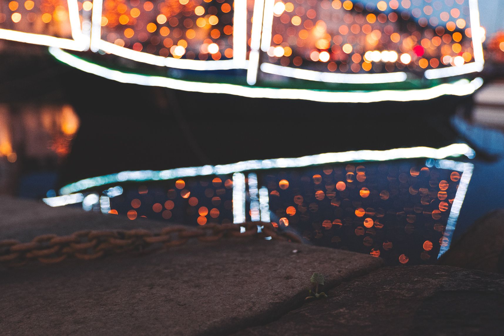 Les décorations de Noël sont de sortie dans le port de Vannes. Le bateau a des voiles faites d'ampoules et de bandes lumineuses. Elles reflètent sur l'eau avec un beau bokeh. En premier plan une chaine de mouillage et le quai