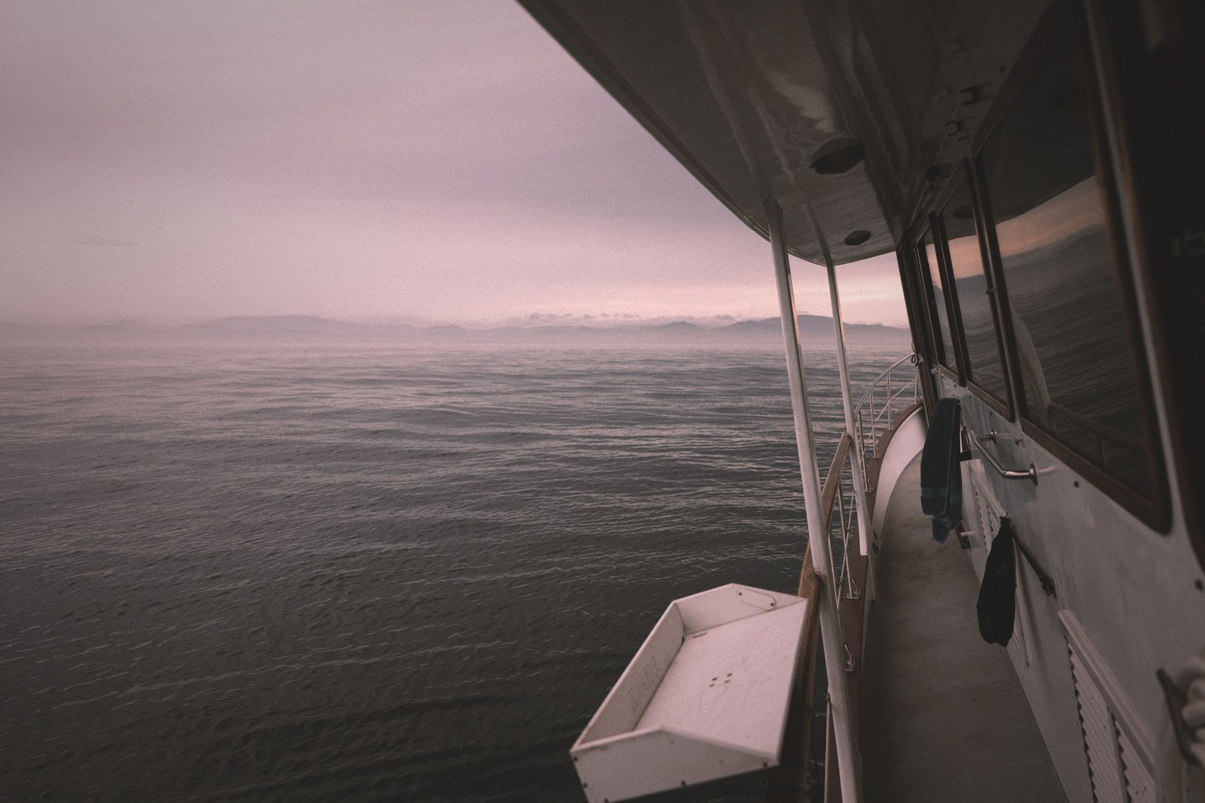 Vue du ponton du bateau, il penche vers la gauche par rapport à l'horizon. Le temps est gris avec le de la brume. Au loin la terre