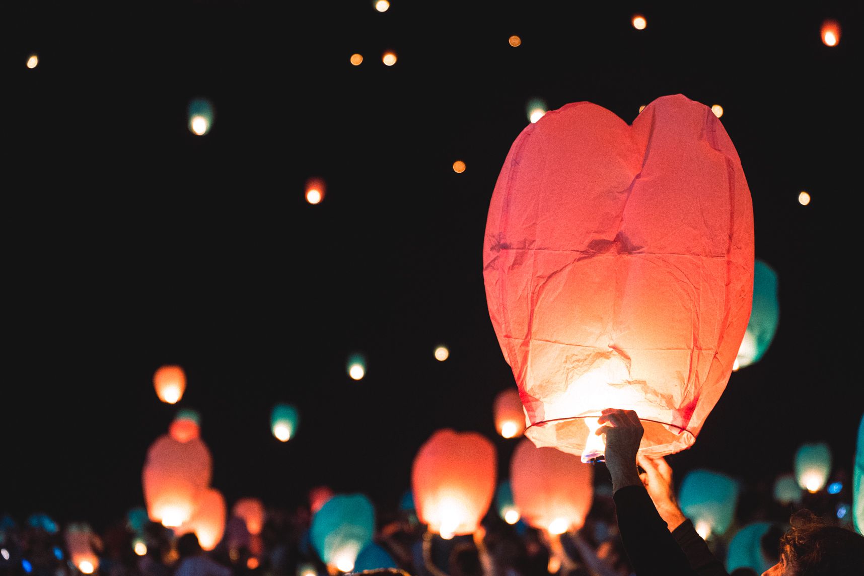 La lanterne rose est gonflée et est prête à s'envoler. Une personne la tiens à bout de bras. Elle forme un coeur. En arrière plan plein d'autres lanternes dans le ciel