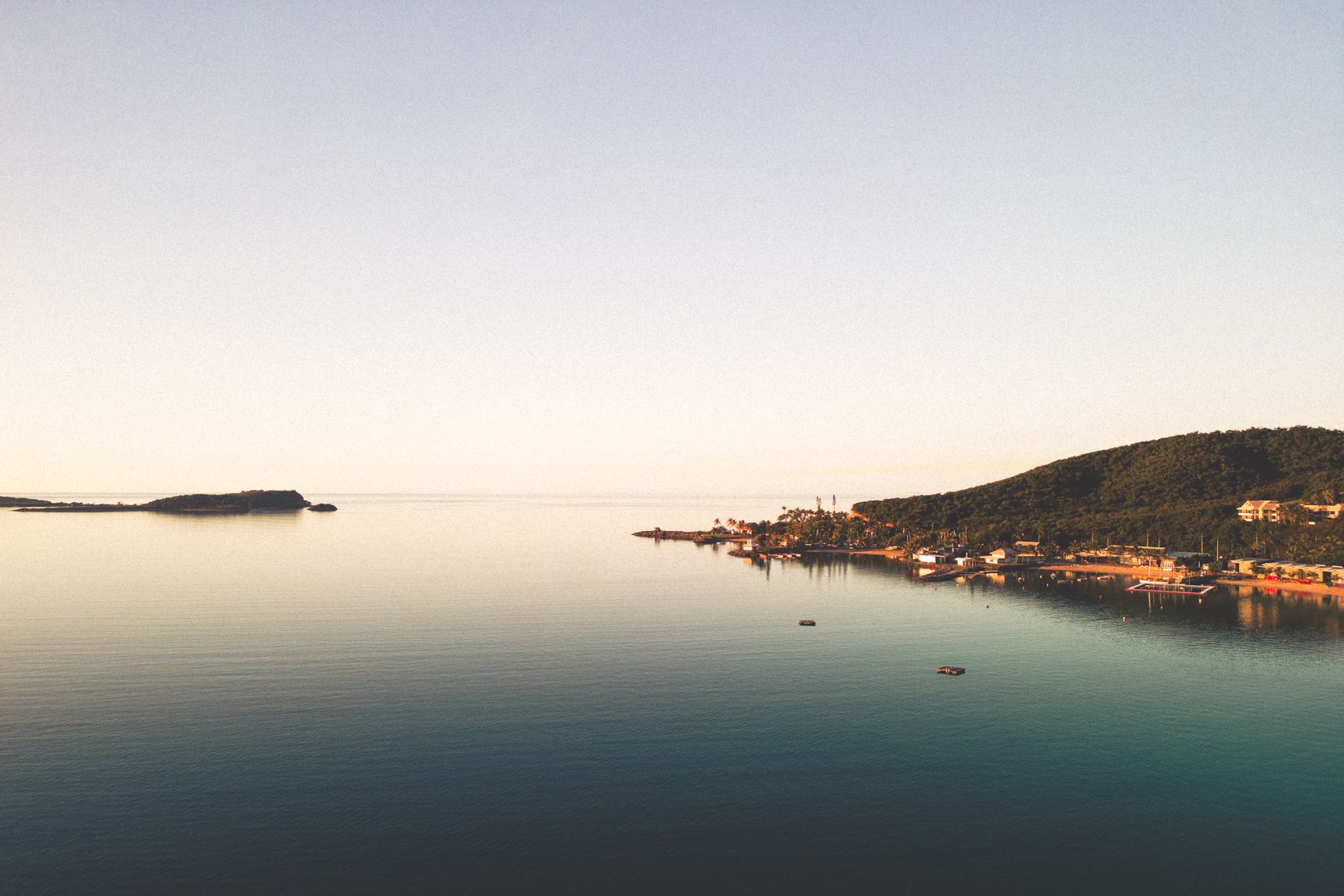 Vue de drone aux premières lueurs du soleil. L'eau est calme, la plage est embrassée par le soleil, les montagnes sur reflètent sur la mer, l'horizon se mélange avec la mer