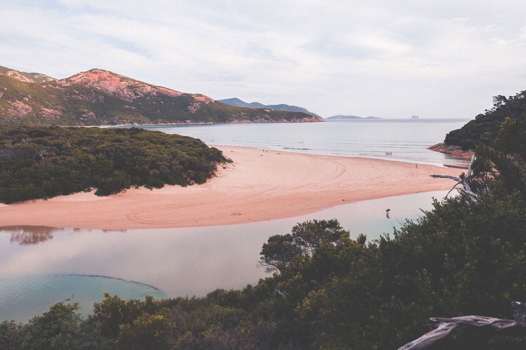 La rivière se jète dans la mer. Elle fait tout le tour de la plage. En premier plan des arbustes et en arrière plan les montages