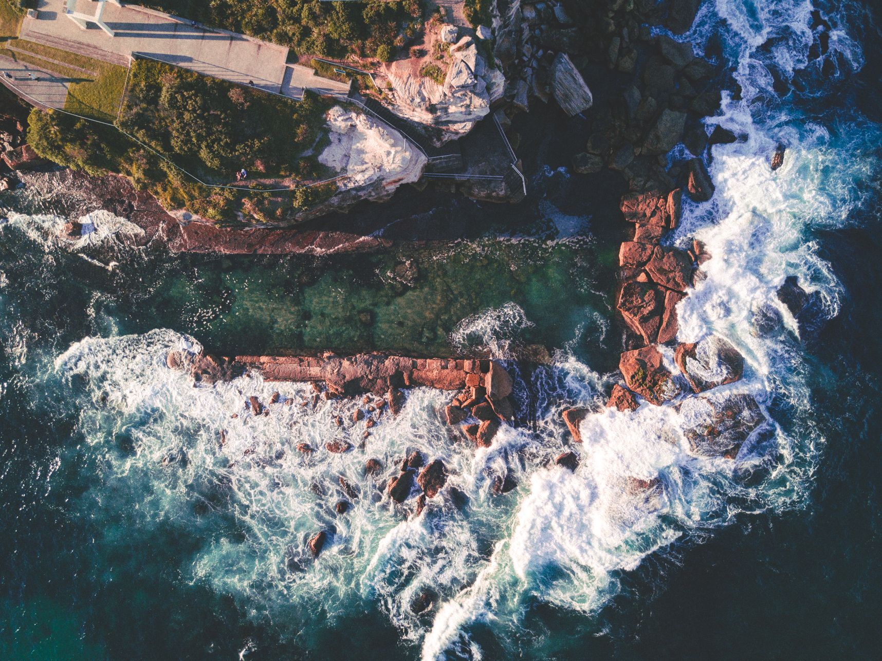 Vue de drone de la piscine d'eau de mer de Coogee, des vagues s'éclatent sur les rochers alors qu'à l'intérieur de la piscine l'eau est calme