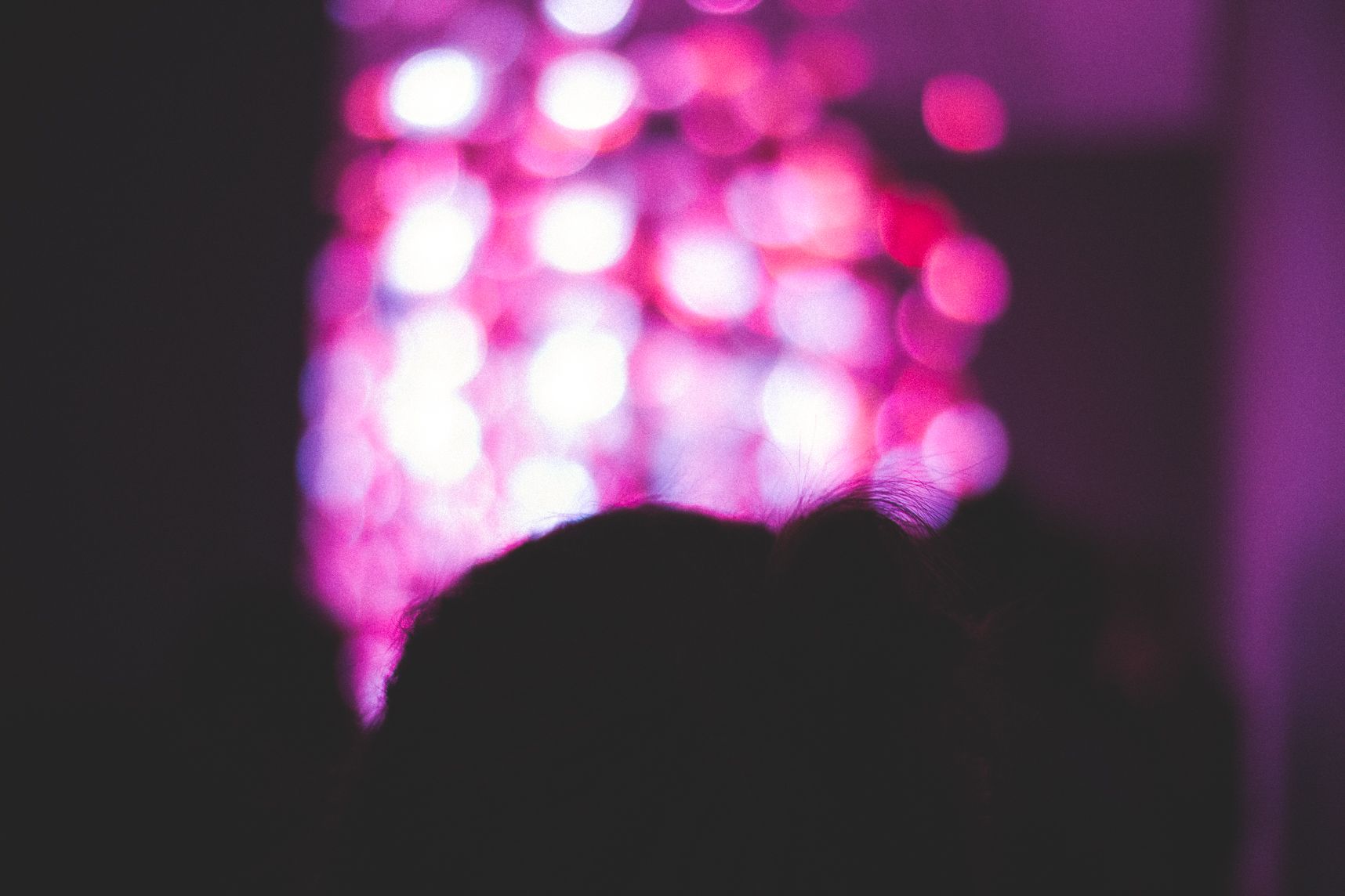 Dans la salle sombre, les lumières hors focus, au dessus de les cheveux de la fille, semblent sortir comme des bulles au dessus de sa tête