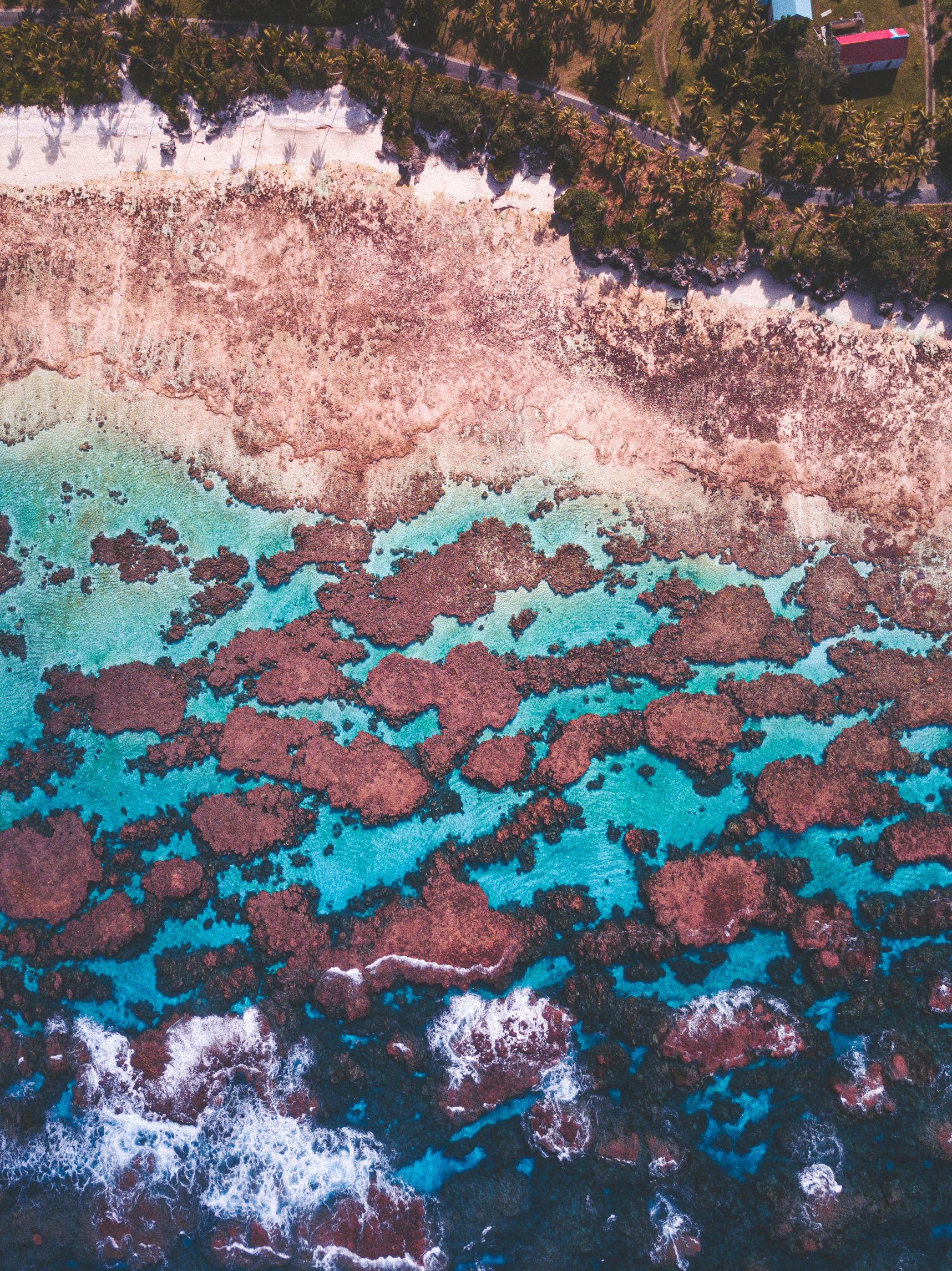 Vue du dessus de la plage de Wabao à Maré. L'eau est turquoise et les vagues montent sur les coraux