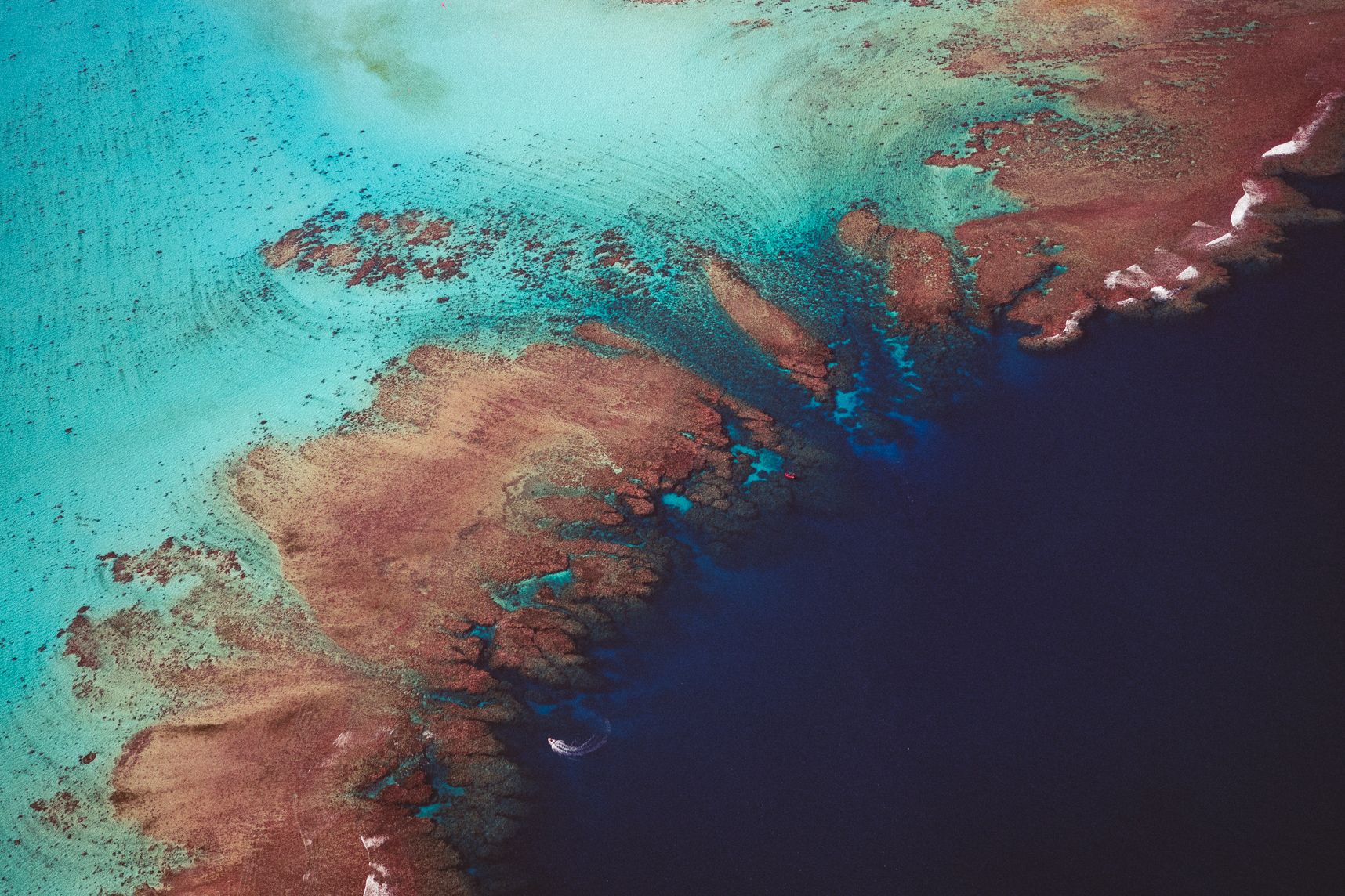 La barrière de corail de Poé vue du ciel. D'un côté les eaux turquoises, de l'autre les eaux profondes. Des bateaux naviguent le long de la barrière