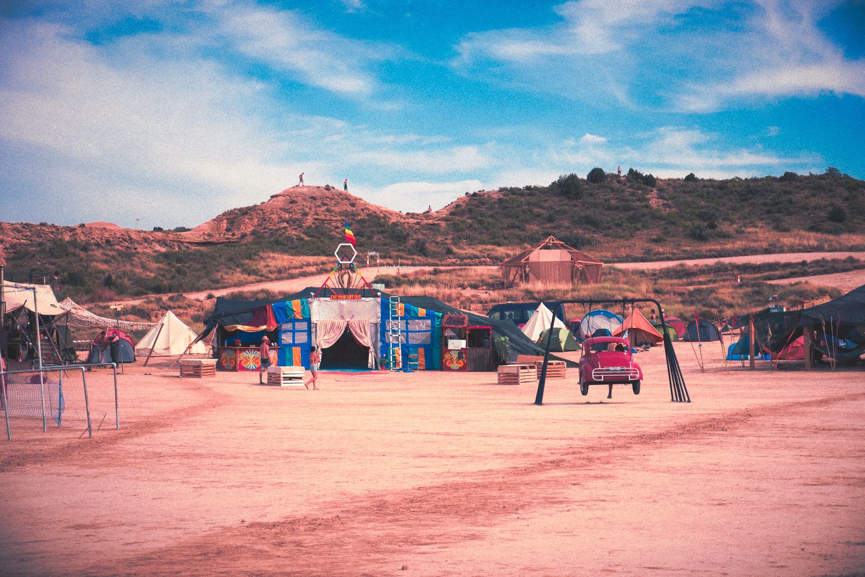 Une partie du festival Nowhere. Une voiture balançoire, des tentes, des barrios, le drapeau LGBT et des gens sur la crête