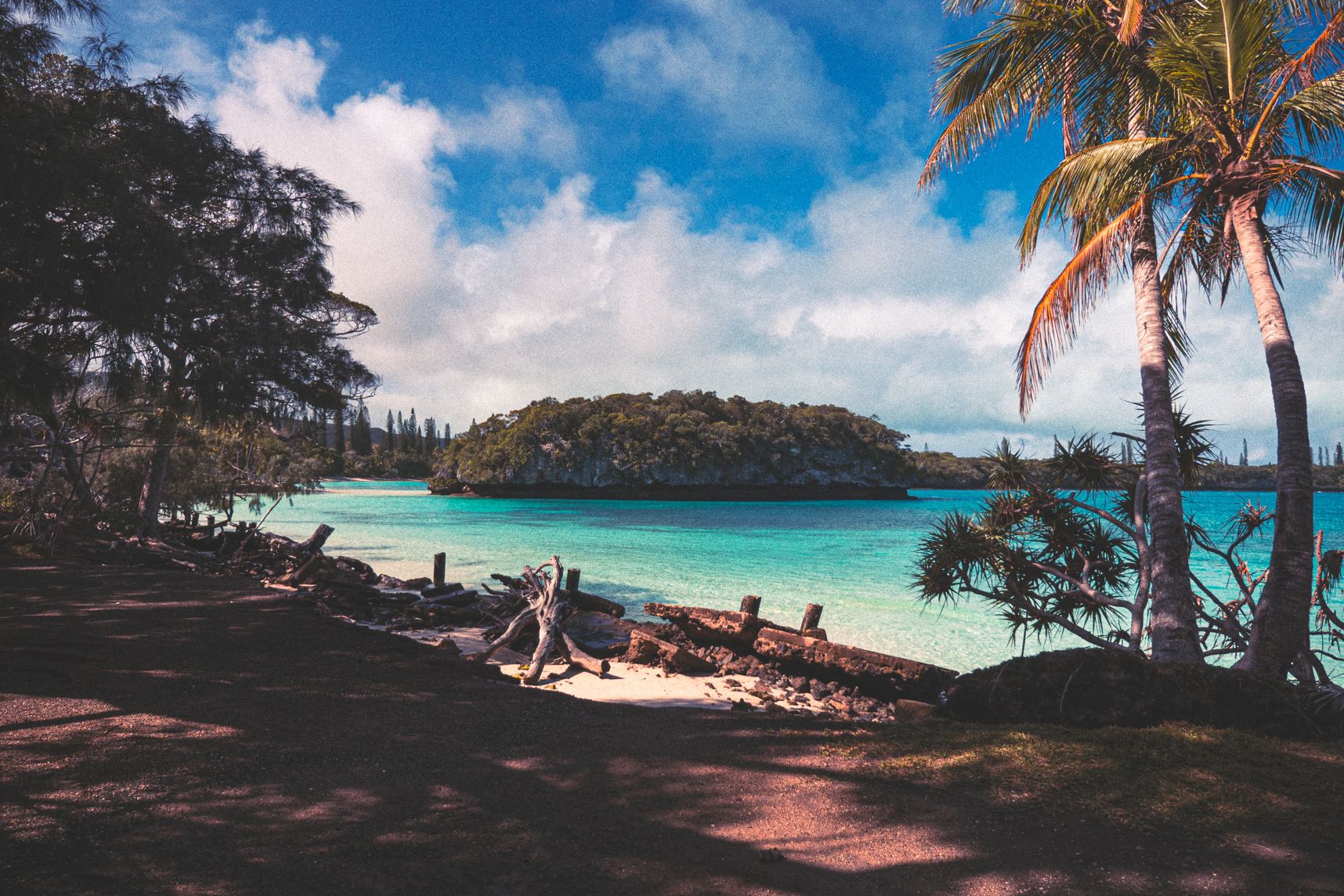 À l'ile des pins, dans une baie, un petit ilot est encerclé par la mer. L'eau est turquoise et la nature flamboyante