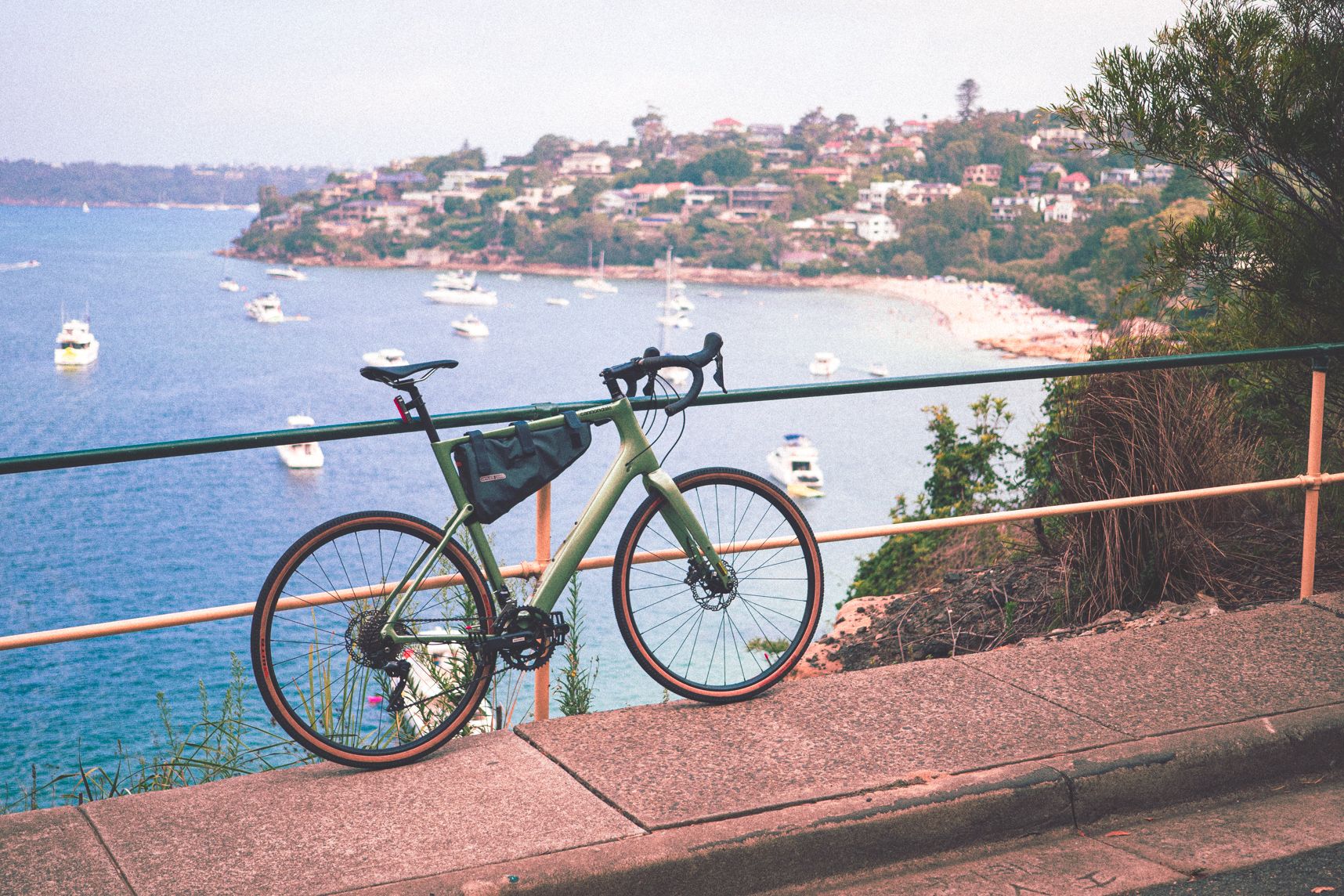 Le vélo Cannondale Topstone Carbon regarde le paysage de Sydney en haut de la côte. On y voit la mer , la plage, les bateaux et les collines voisines