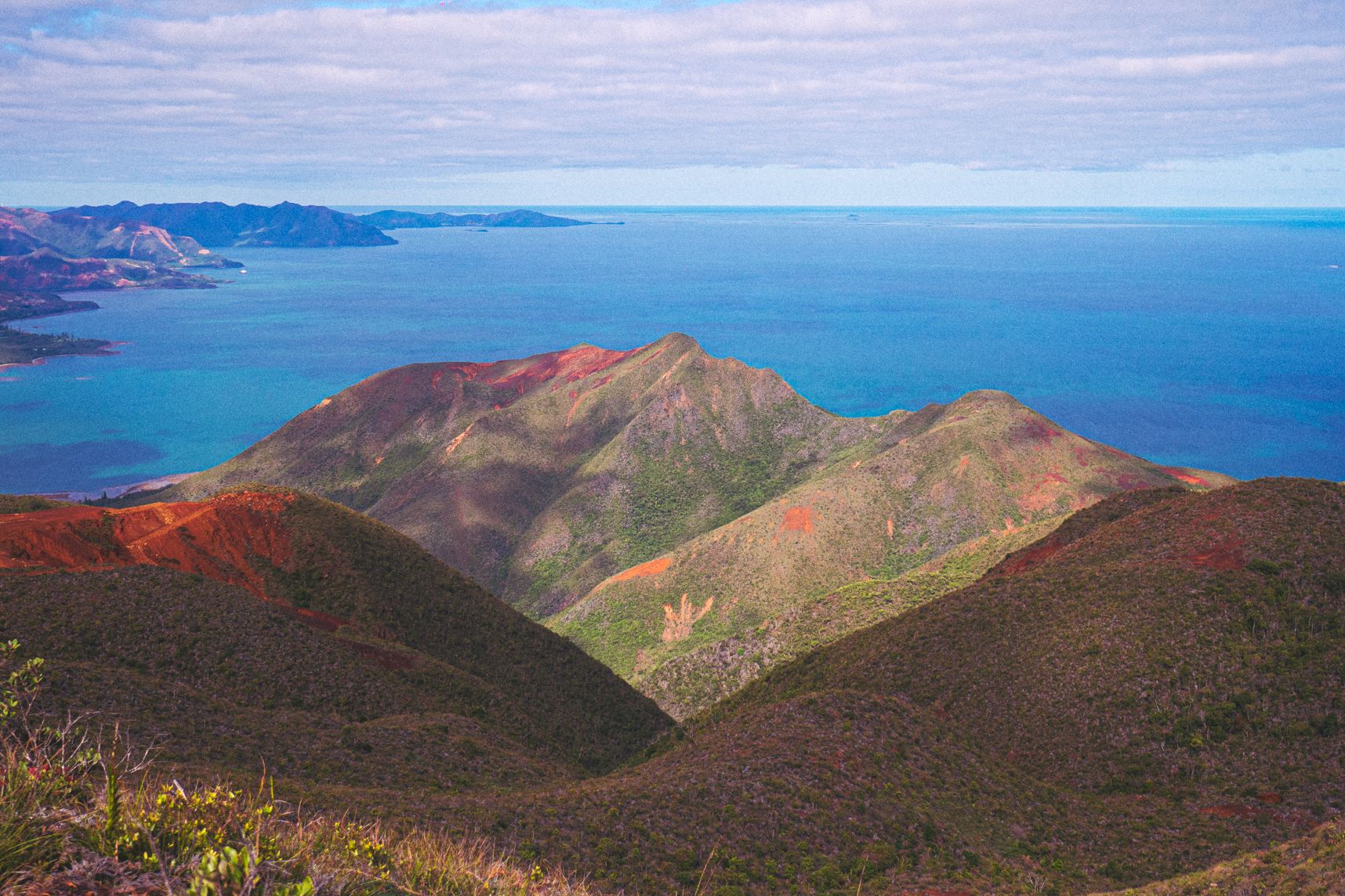 Point de vue en haut du Mont Dore, les montagnes en premier plan, la mer turquoise en second. Au milieu de la montagne comme une trace de pas de dinosaure 