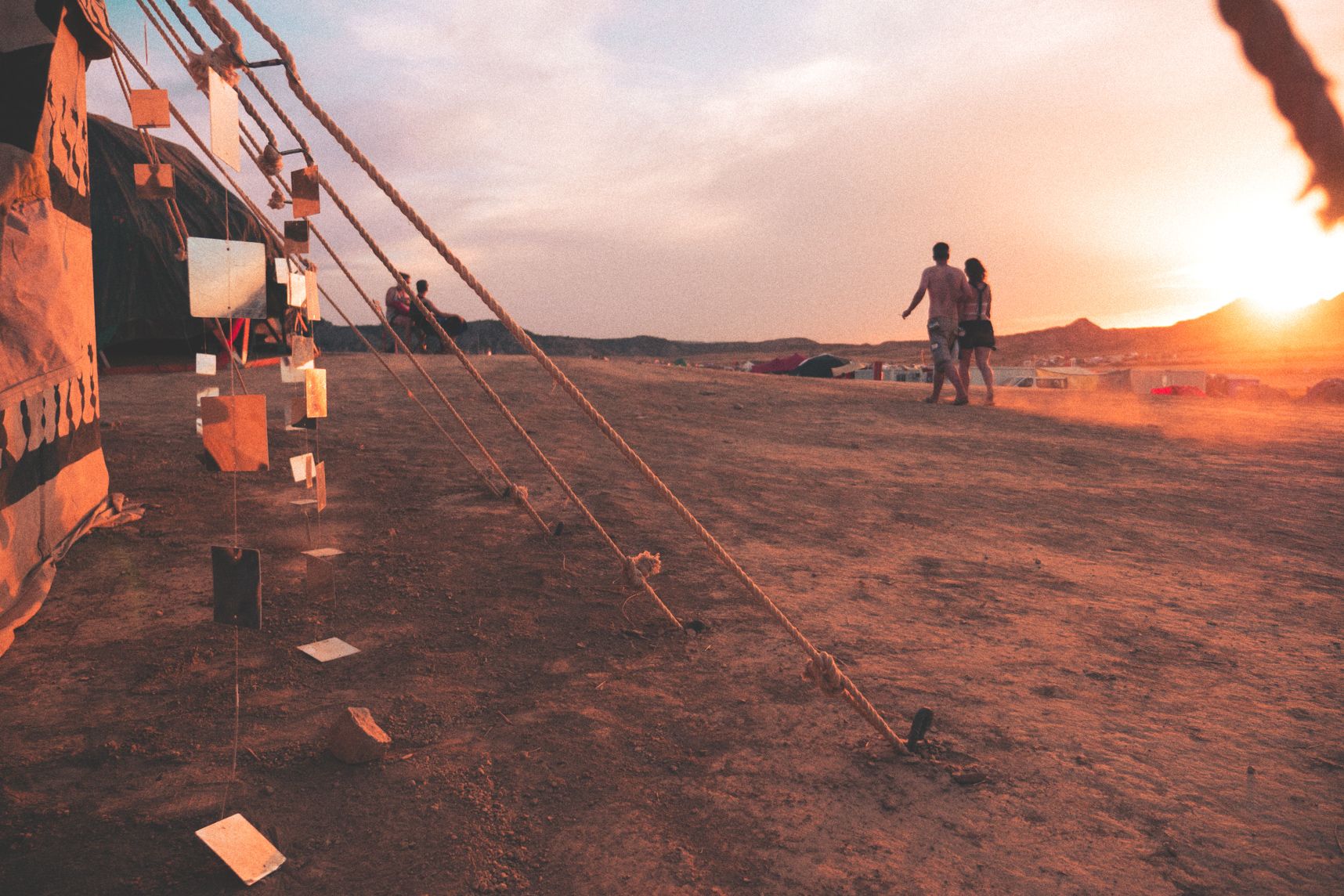 Coucher de soleil au festival Nowhere, deux amoureux marchent sur la playa et des miroirs au premier plan reflètent le soleil