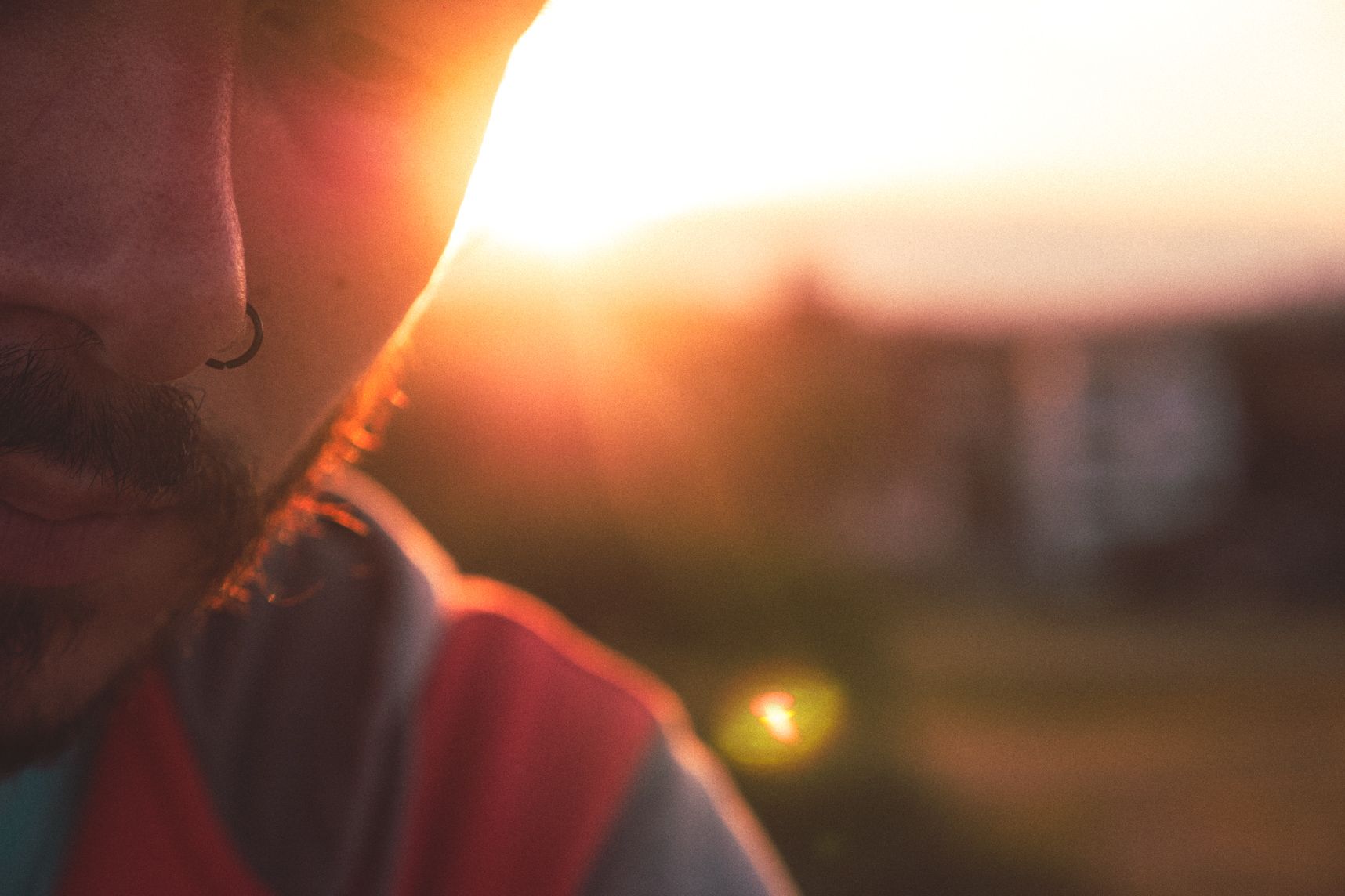 Une moitié de visage regardant vers le bas, un piercing à la narine, le coucher de soleil et Sydney en fond