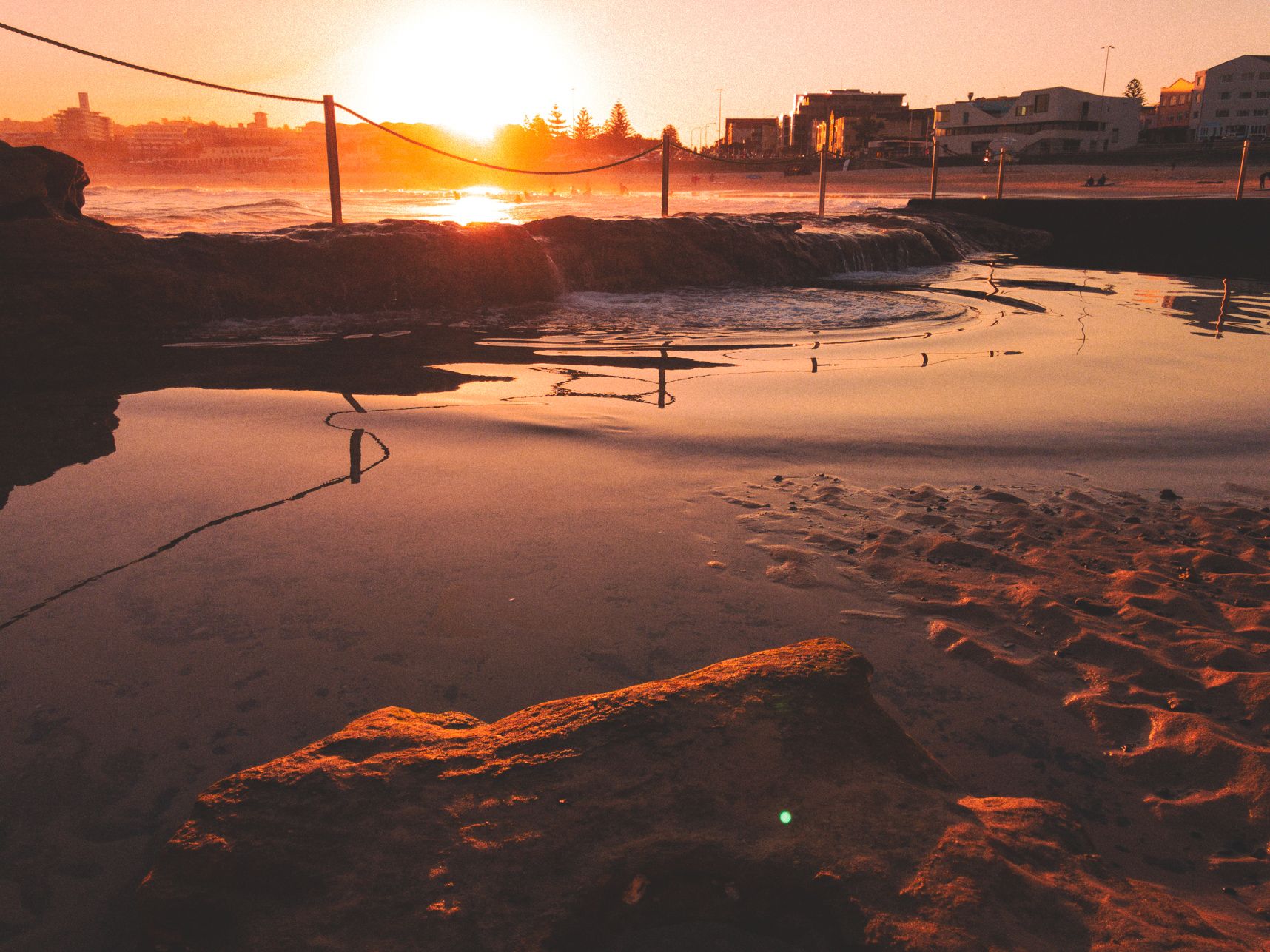 Coucher de soleil à Bondi Beach. Le soleil reflet sur la mer alors qu'une vague arrive sur la piscine d'eau de mer. formant des ondulations