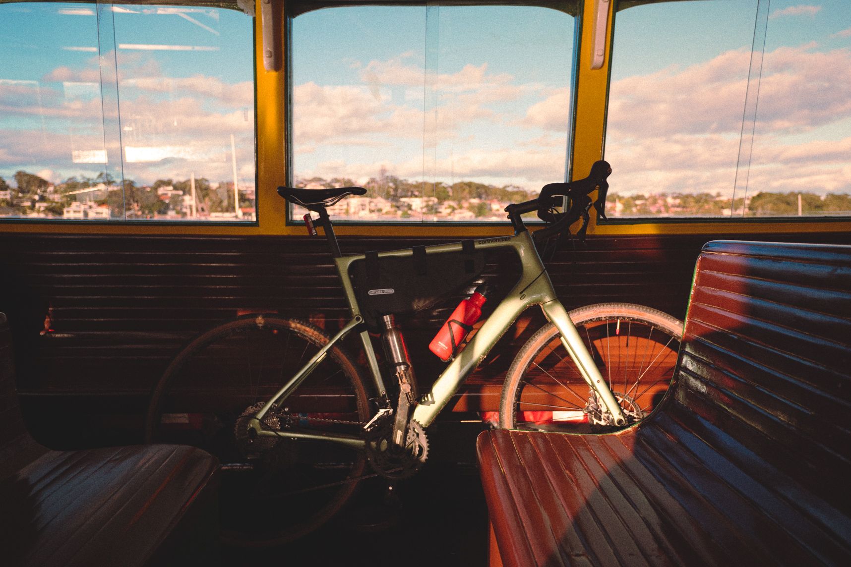 Pour la traversée en bateau, le vélo prend la place d'un passager. Le soleil rasant illumine une part du vélo. Avec ses bidons, le vélo est plein de gadoue. Le paysage à travers les fenêtres est flou