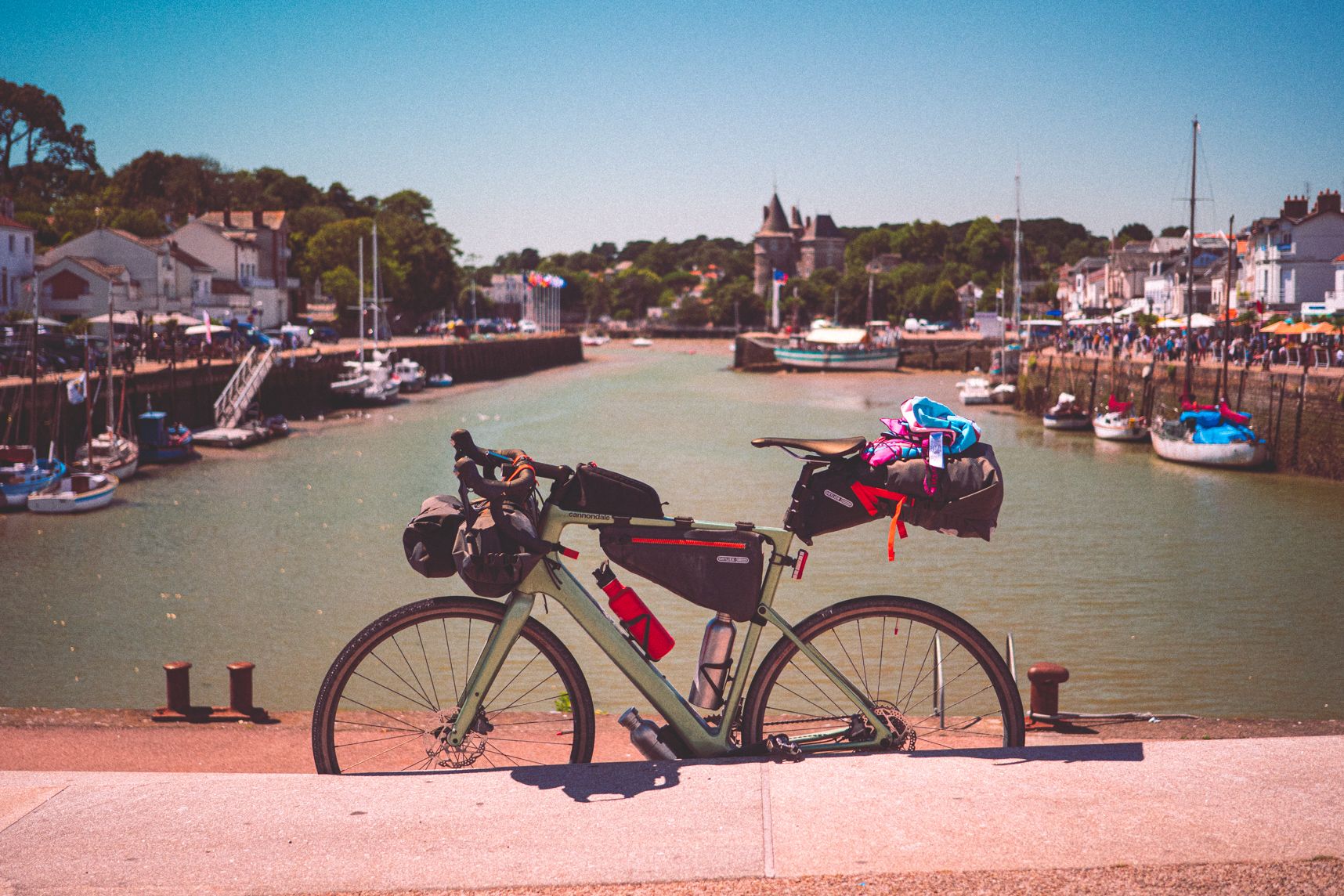 Sur le premier plan un vélo gravel monté avec ses affaires de bikepacking. En arrière plan le port de Pornic sous le ciel bleu
