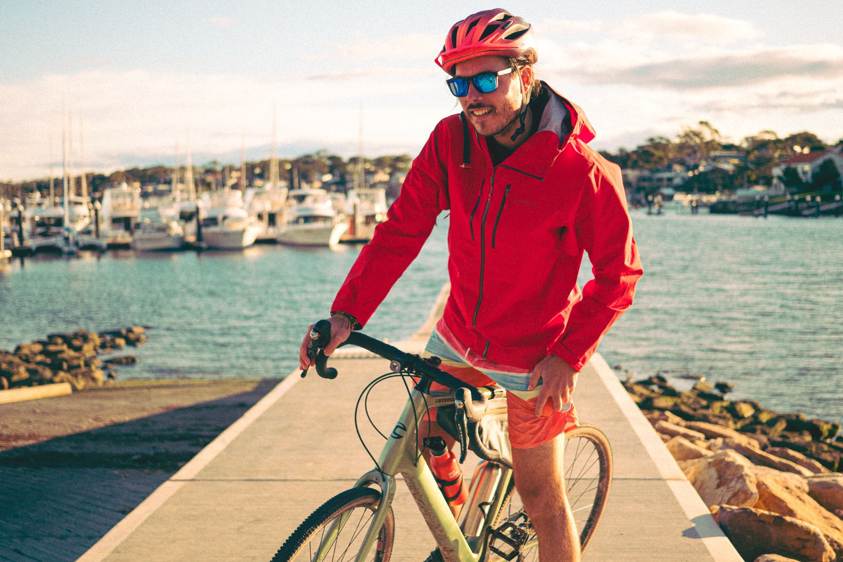 La personne sur le vélo a un manteau rouge flamboyant, elle pourrait être le père Noël. En arrière plan le port de Cronulla, ses bateaux et la cale de mise à l'eau
