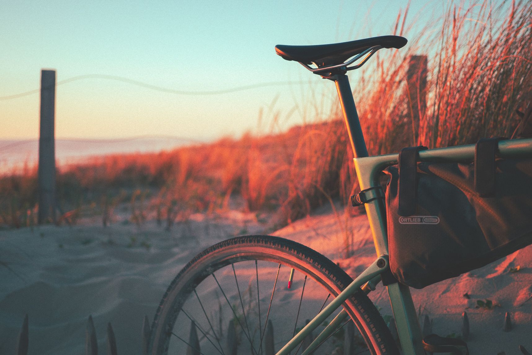 La selle et une partie de la roue arrière du vélo posées sur la dune. Le coucher de soleil leur donne des tons orangés