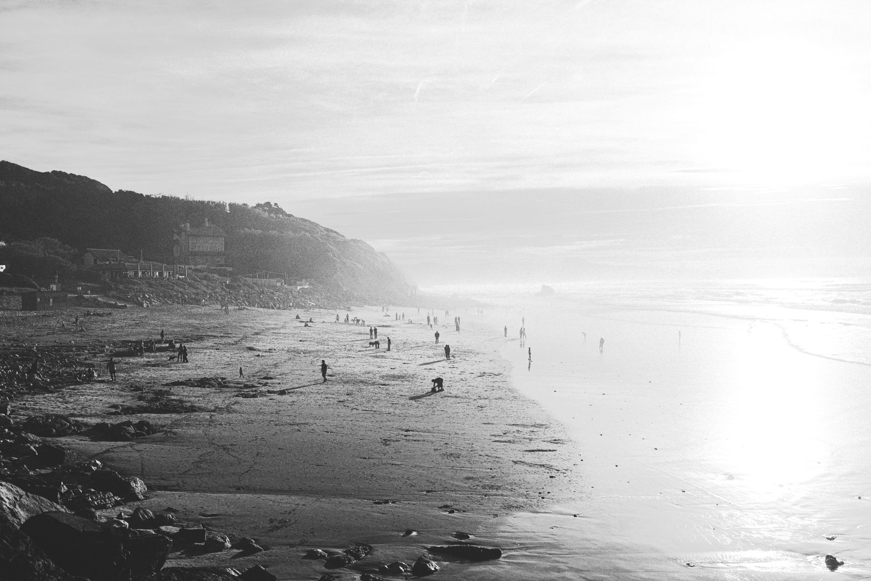 Photo en noir et blanc d'une plage de Biarritz au moment du coucher de soleil. A gauche la plage et à droite la mer. Plein de gens sur la plage qui forment des petits points. Les ombres des gens sont longues