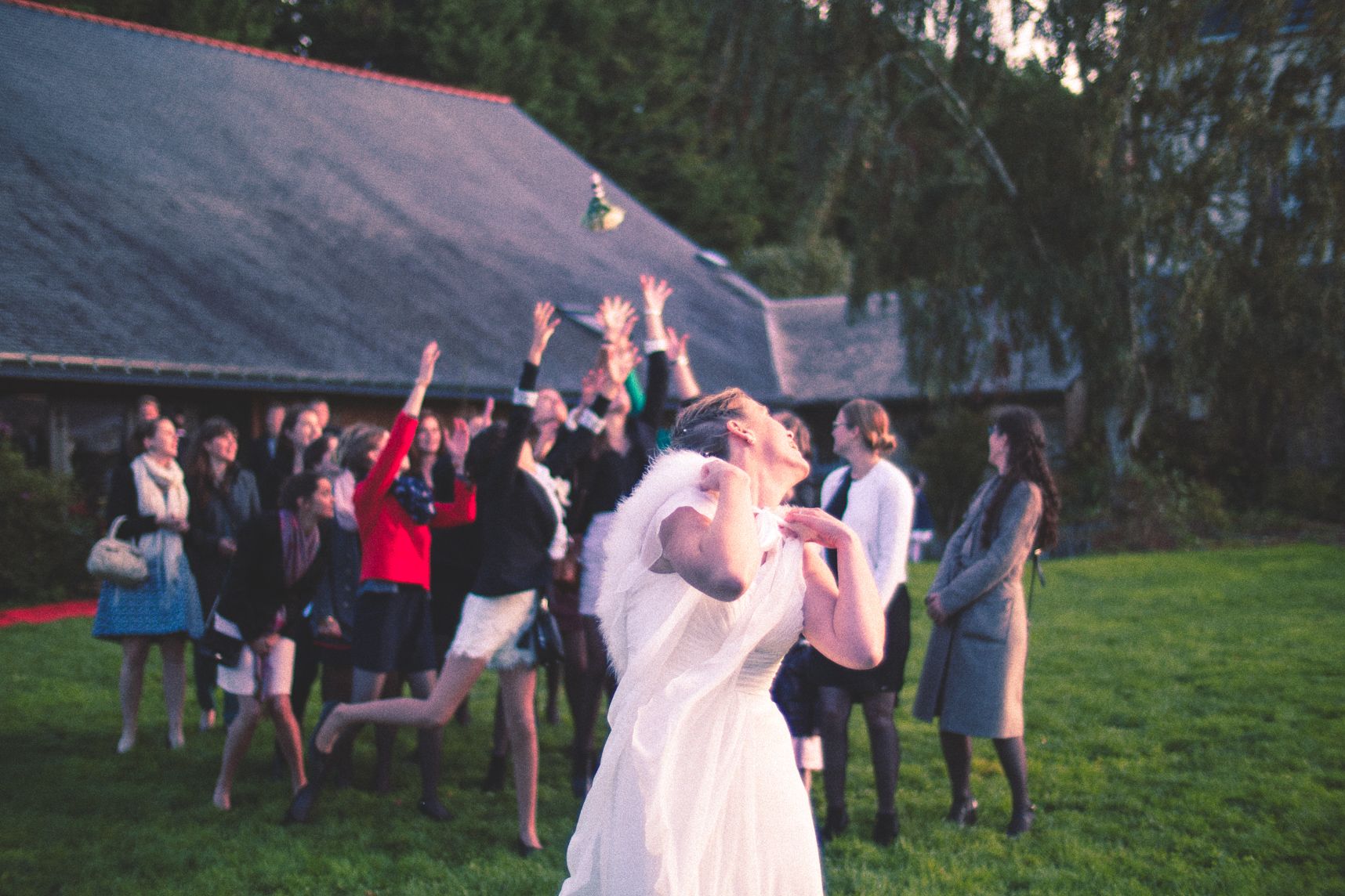 La mariée jette son bouquet dans la foule derrière. Plusieurs personnes lèvent les bras et tentent de le rattraper