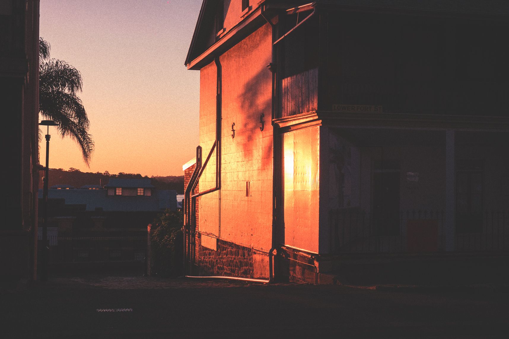 En haut de The Rocks, le coucher de soleil reflète sur le mur d'une maison. L'allée surplombante laisse apercevoir le paysage
