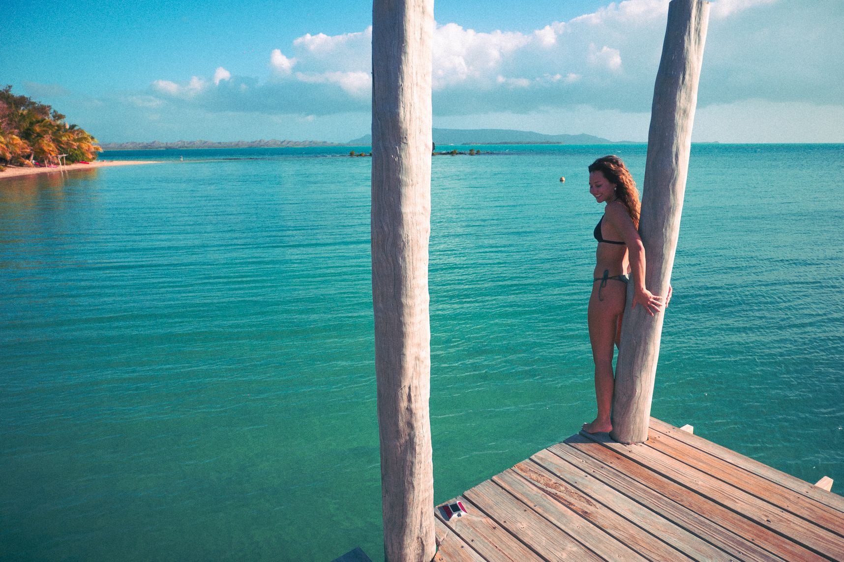 Au bout du pontonune femme s'accroche au pilier en bois. L'eau est turquoise et les montagnes bordent le paysage