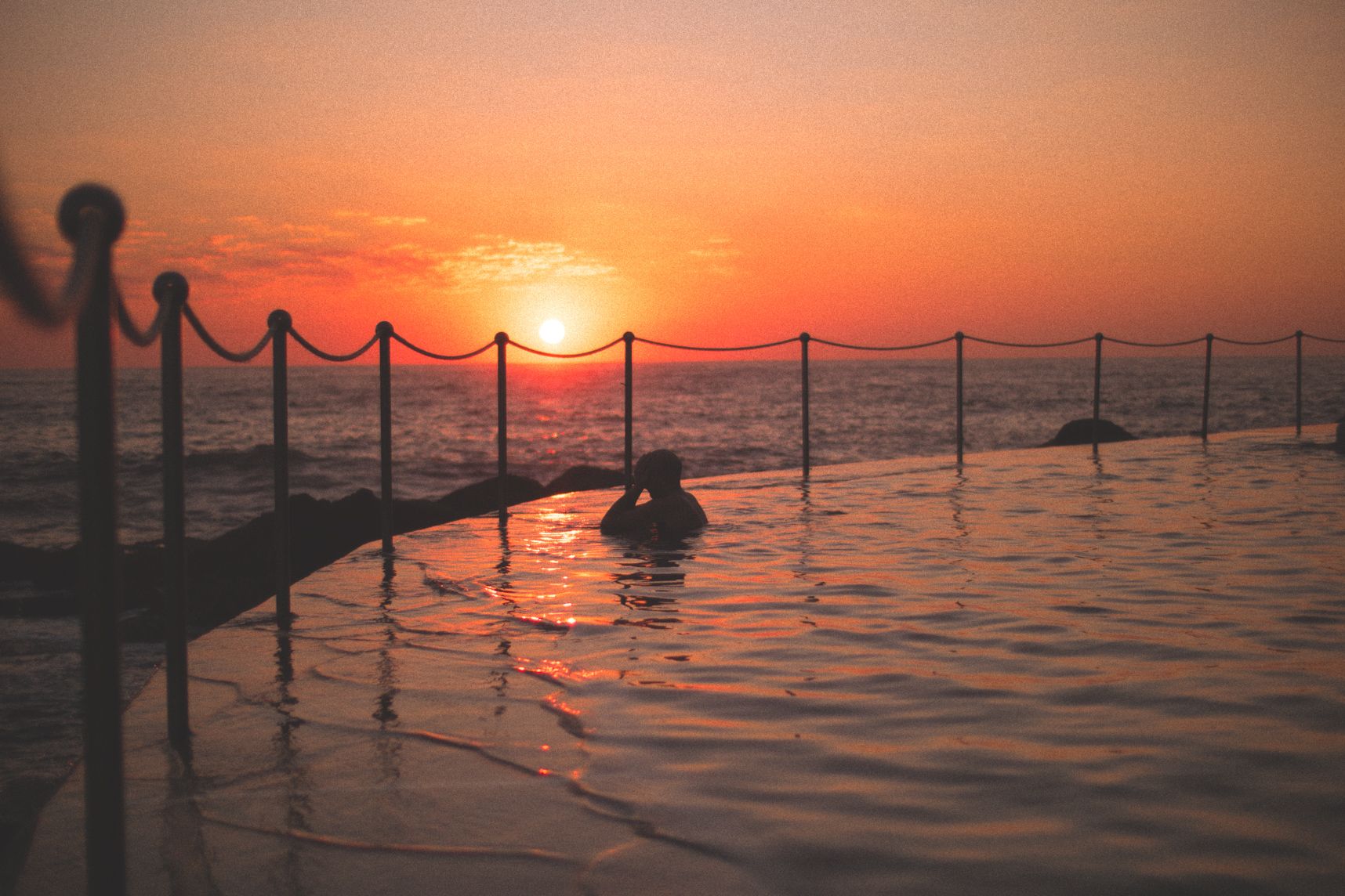 Lors du lever de soleil sur la piscine de Bronte, les mains sur sa tête, un homme admire le paysage