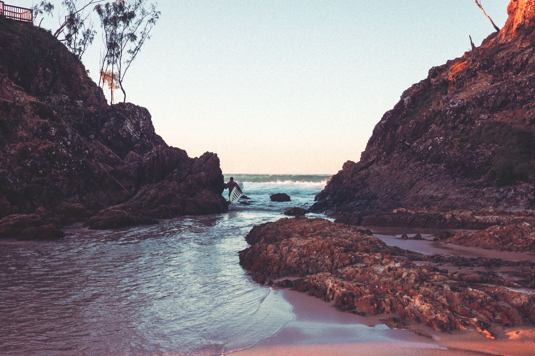 À Byron Bay, un surfeur s'engouffre entre deux gros rocher pour aller chercher les vagues