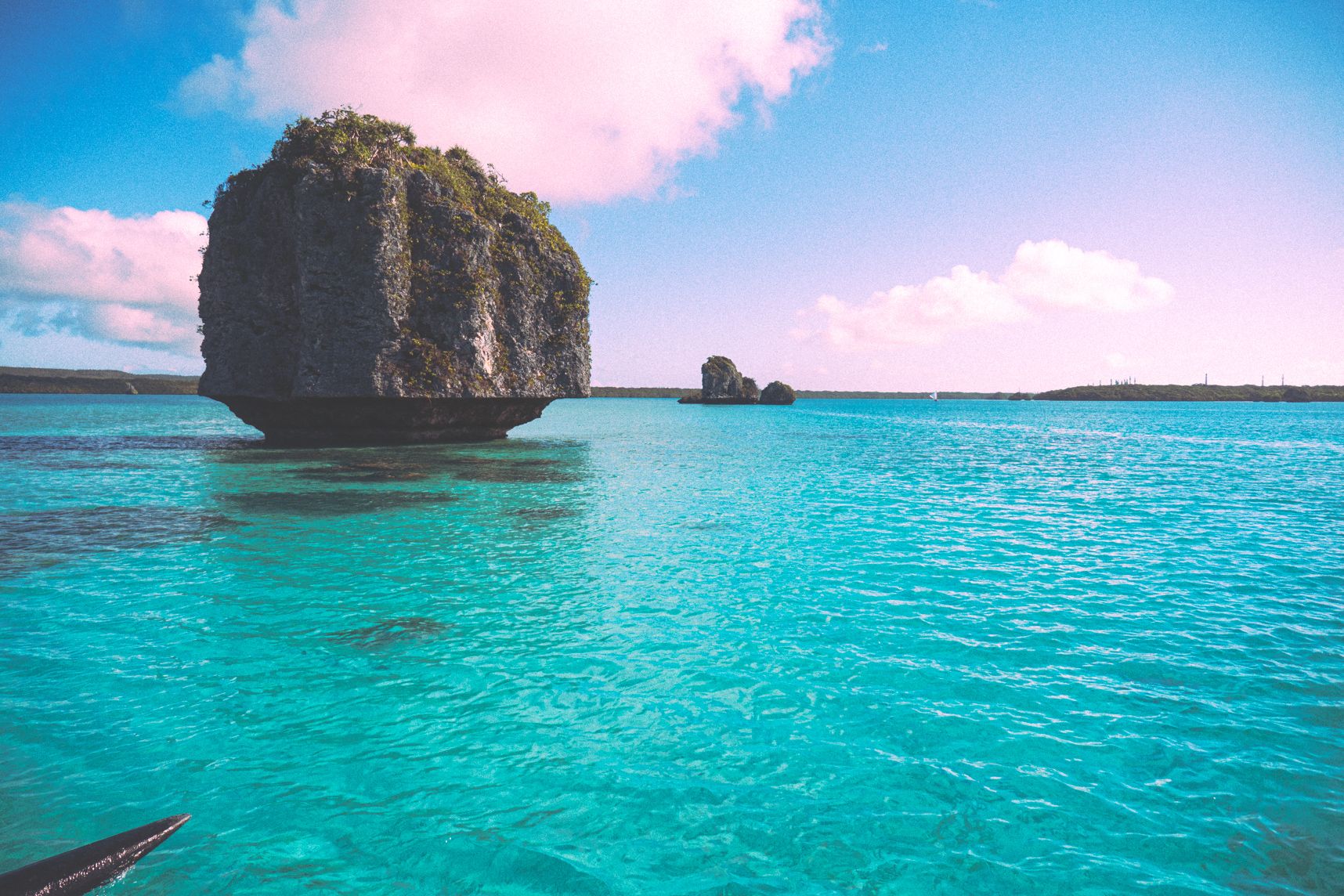 Dans la baie d'Upi l'eau est turquoise. Des rochers sont en plein milieu, seul