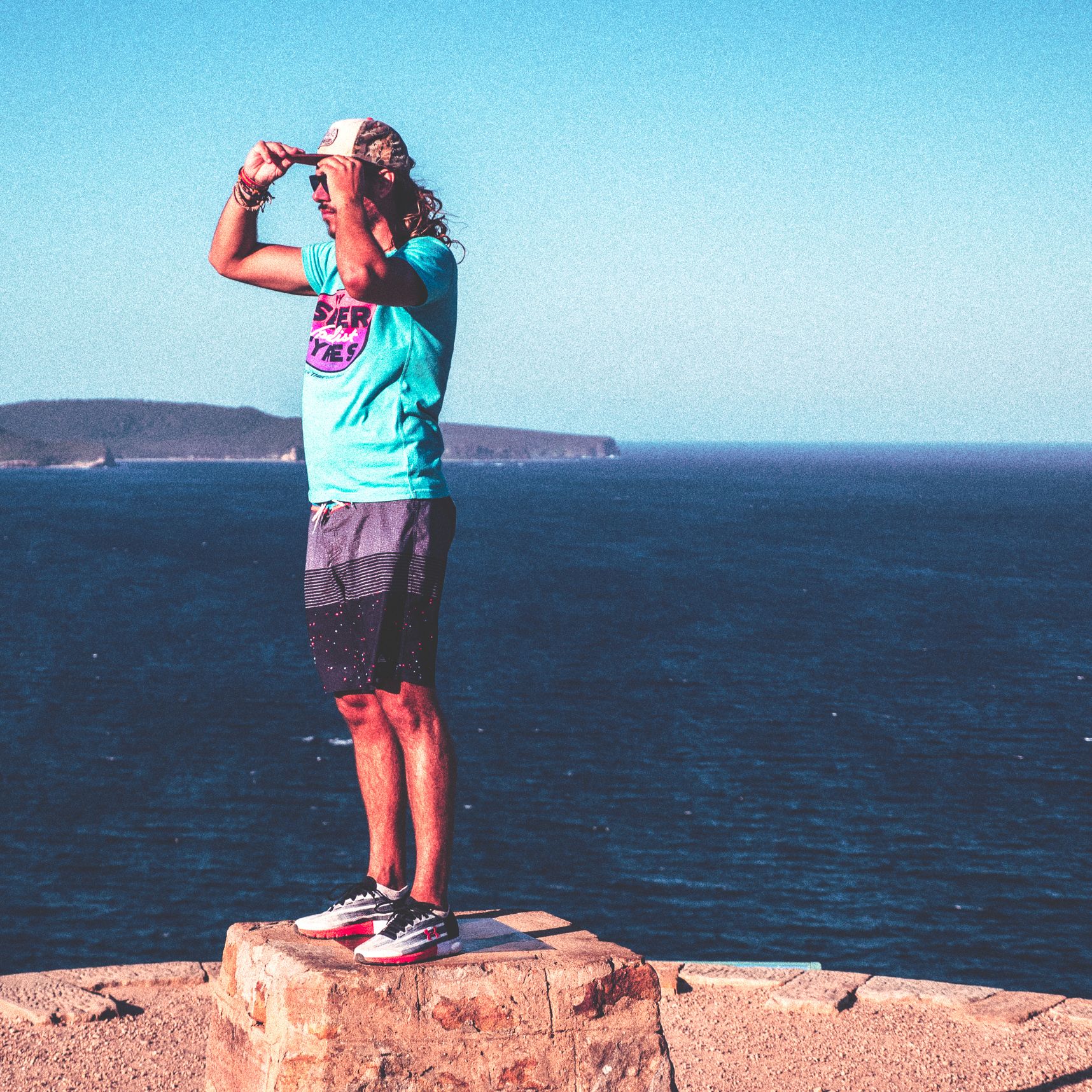 Auto portrait sur un muret, mains sur la casquette cheveux au vent, la mer vue du phare de palm beach