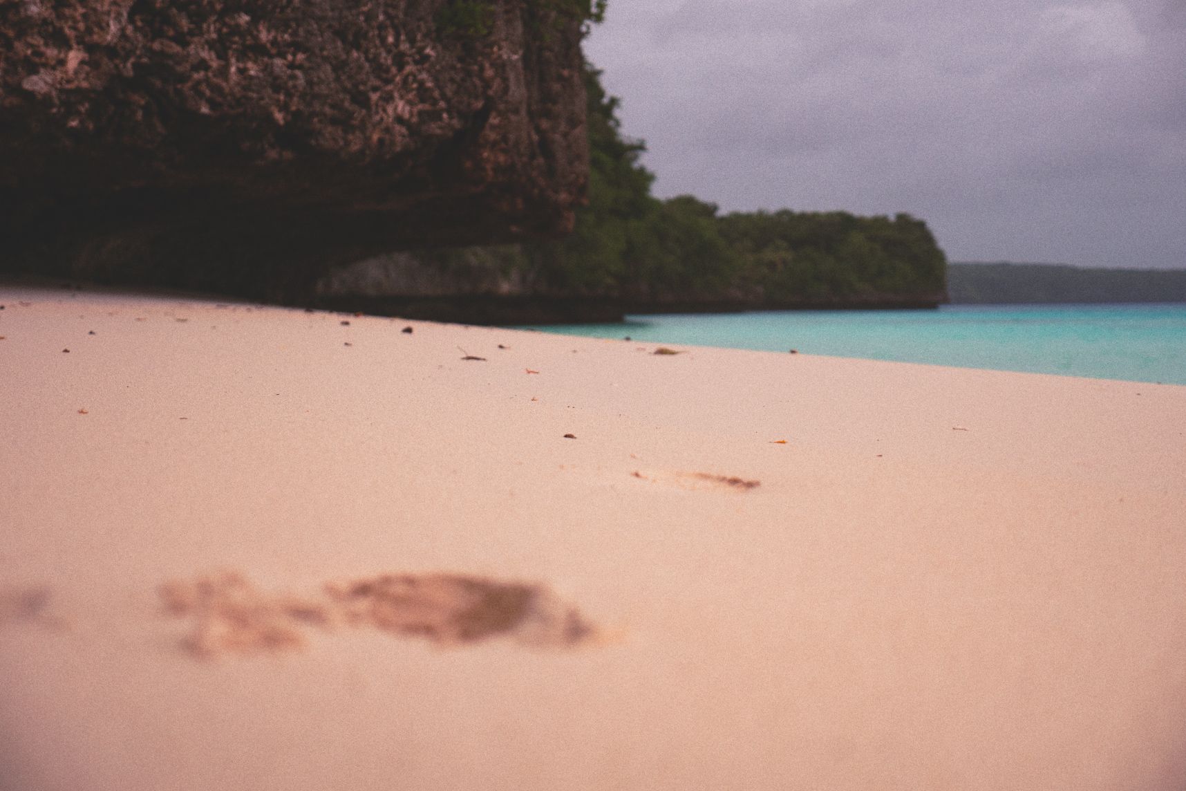 Une plage déserte de Lifou, une trace de pas dans le sable, l'eau turquoise et les falaises en arrière plan
