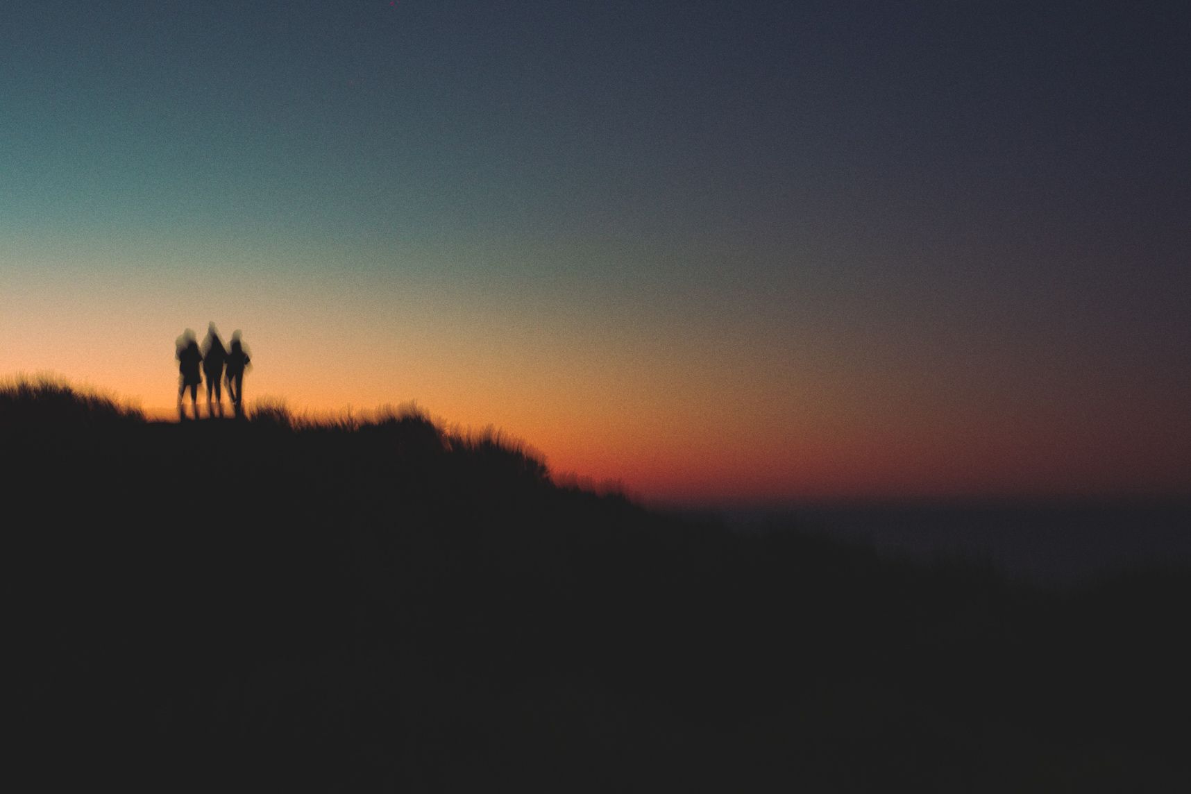 Derrière le rocher le soleil se lève. Dessus, trois personnes l'attendent avec impatience 